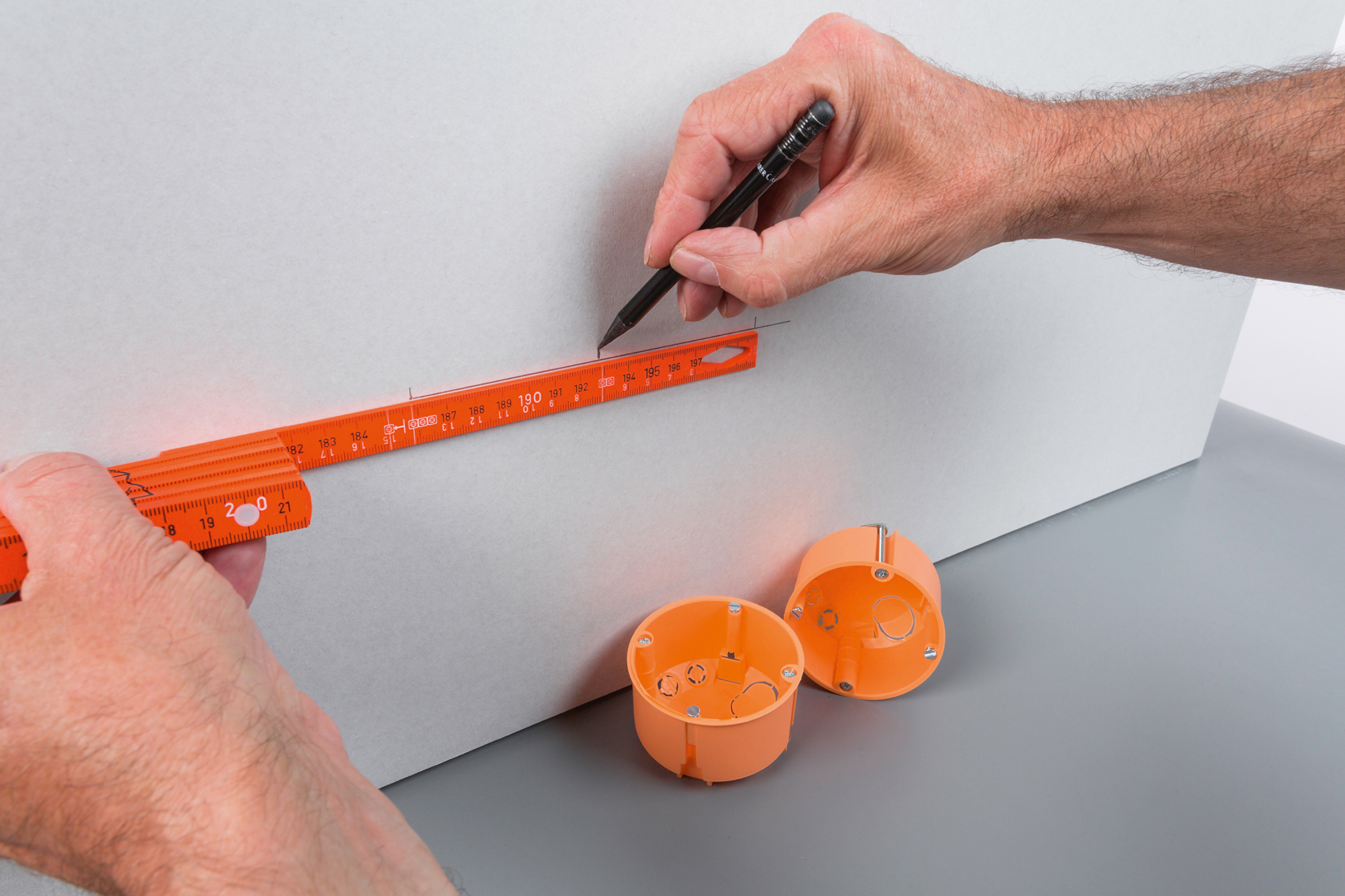 Hände messen und markieren eine Wand mit einem orangefarbenen Lineal und Bleistift und zwei Dosen.