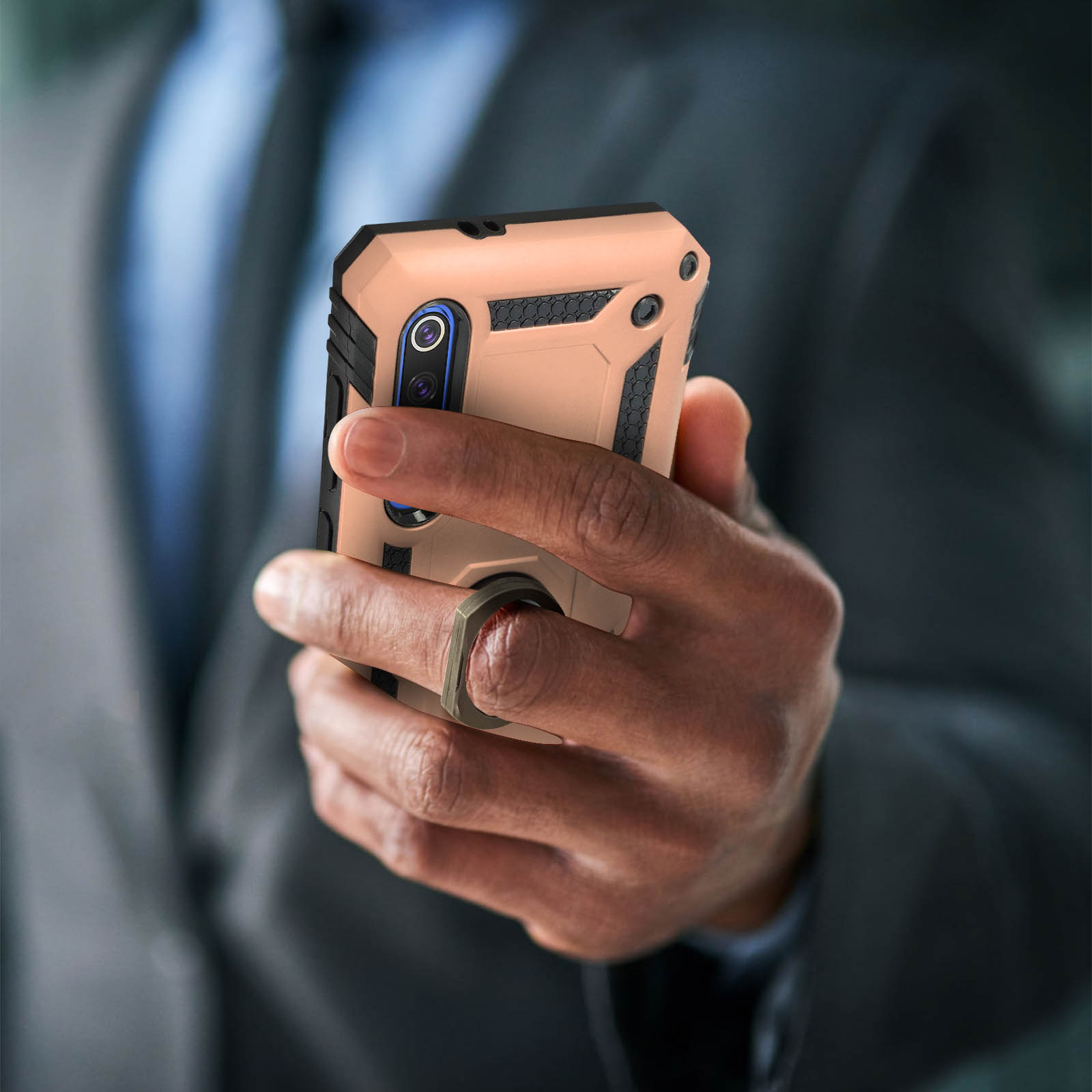 Mano che tiene un telefono con una custodia marrone e nera. Lo sfondo mostra un abito.