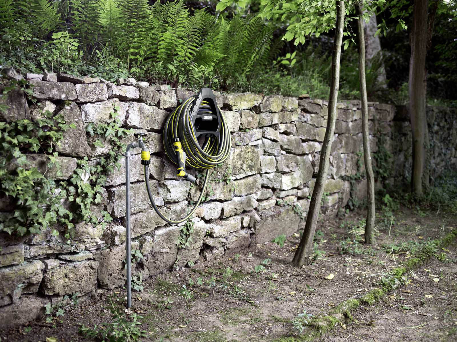 Ein Gartenschlauch ist an einer Steinmauer mit Wasserhahn und Farn im Hintergrund montiert.