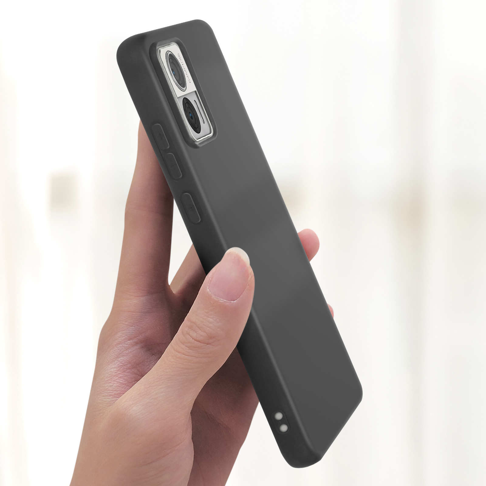 Mano che tiene un telefono nero con sporgenza della fotocamera. Il telefono ha una finitura opaca. Lo sfondo è sfocato.