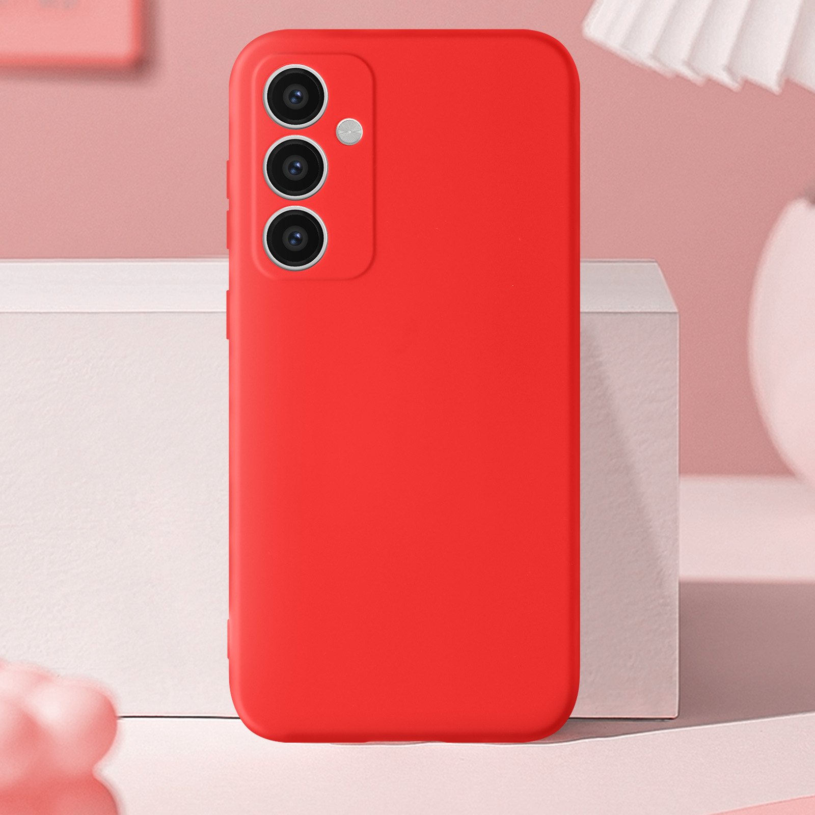 Custodia rossa per telefono con tre fotocamere. Superficie bianca, sfondo rosa.