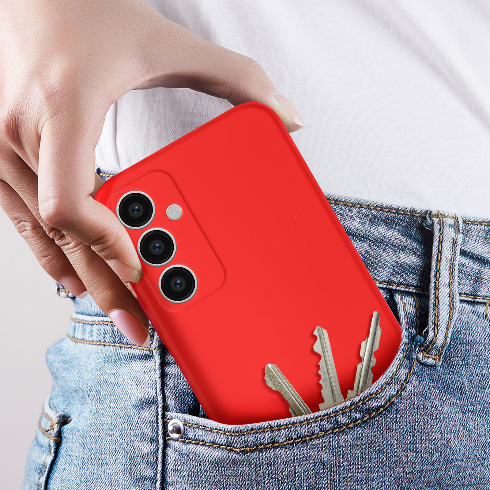 Custodia rossa per telefono in una tasca dei jeans, con chiavi in tasca. Lo sfondo è bianco.