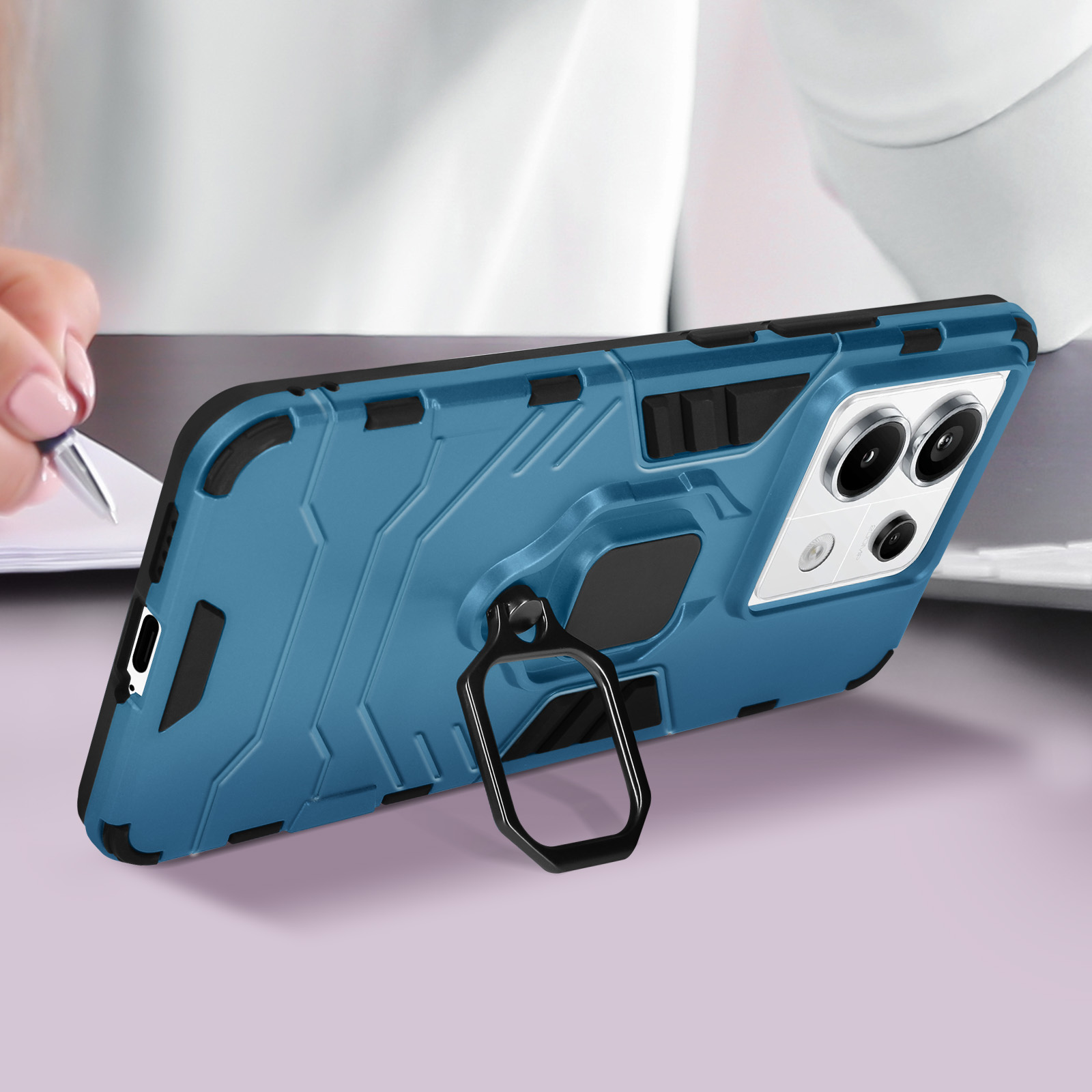 Una custodia blu per telefono con un supporto ad anello, appoggiata a una scrivania. Una persona che scrive sullo sfondo.