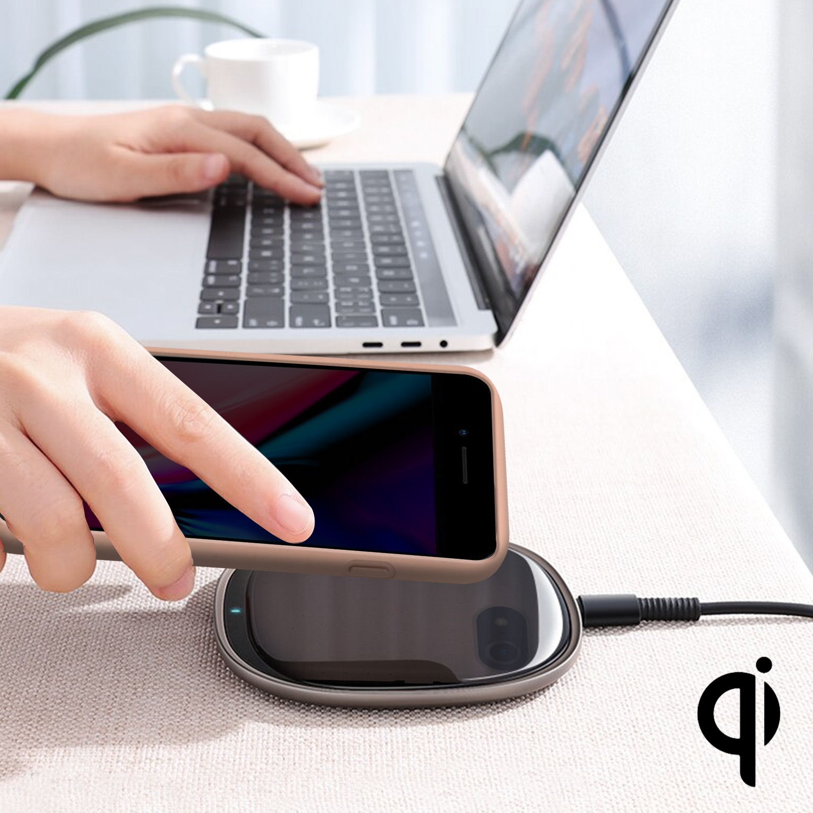 Una persona che usa un telefono con una custodia su un caricatore wireless accanto a un laptop.