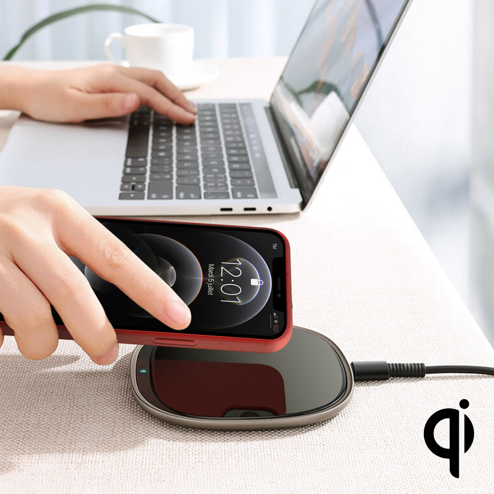 Un telefono rosso si carica su un caricatore wireless. Un laptop sullo sfondo.