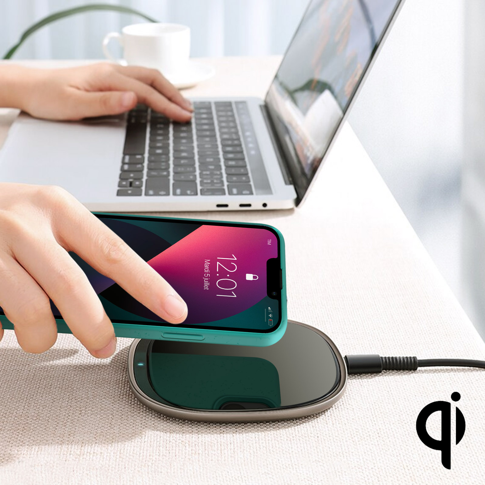 Un telefono su un caricabatterie wireless. Una mano posiziona il telefono sul caricabatterie. Un laptop è visibile.