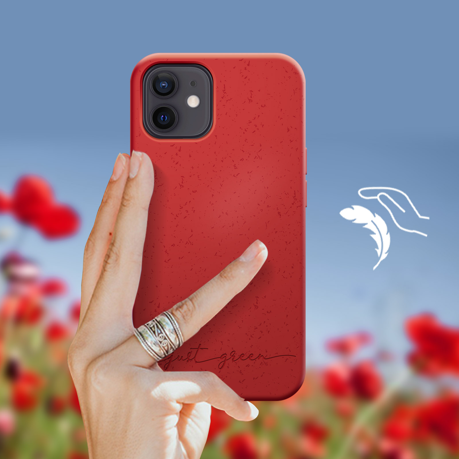 Mano che tiene una custodia rossa con testo 'just green', contro un campo di papaveri sfocato e cielo blu.