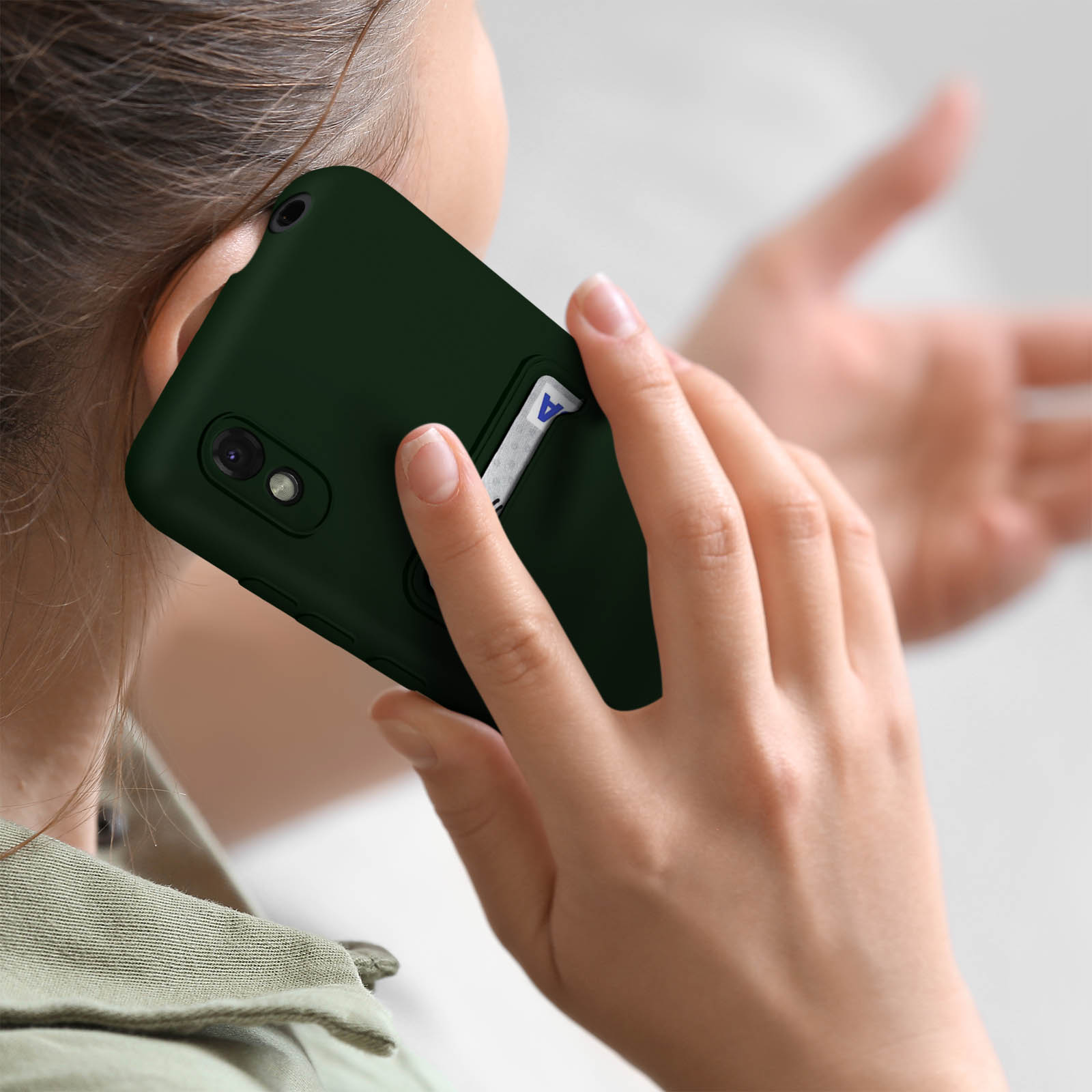 Una persona che tiene un telefono verde scuro all'orecchio, con una carta bianca sul retro.