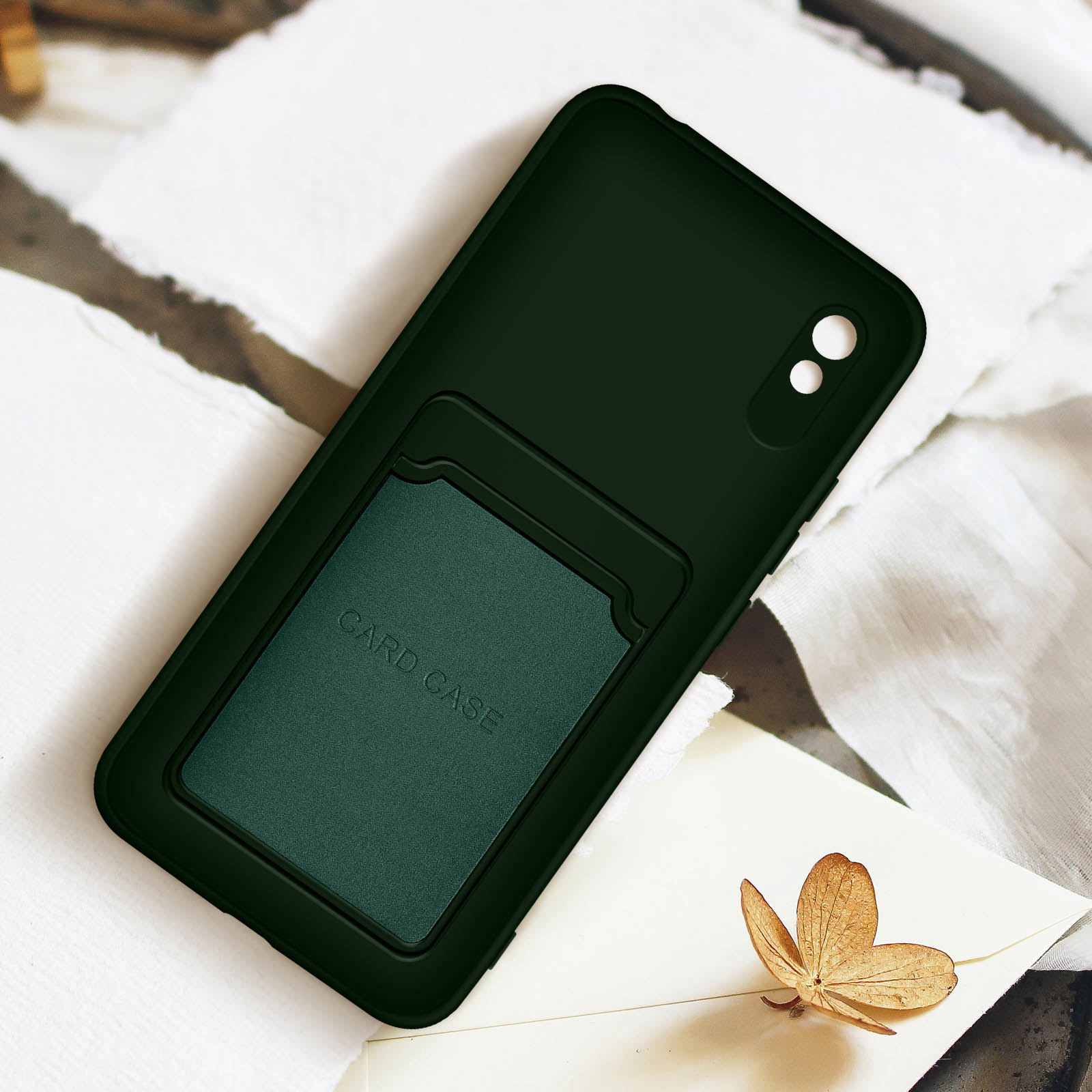 Custodia per telefono verde scuro con porta carte su superficie bianca, con fiore dorato.