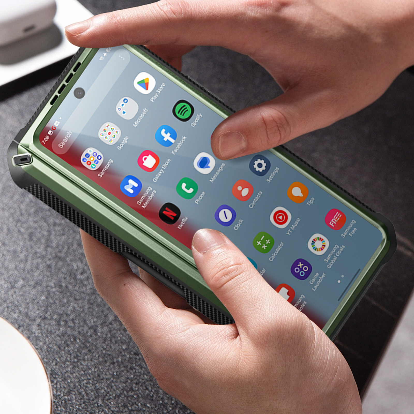 Una persona che tiene un telefono con una custodia verde. Lo schermo mostra le app. La custodia ha una cornice nera.