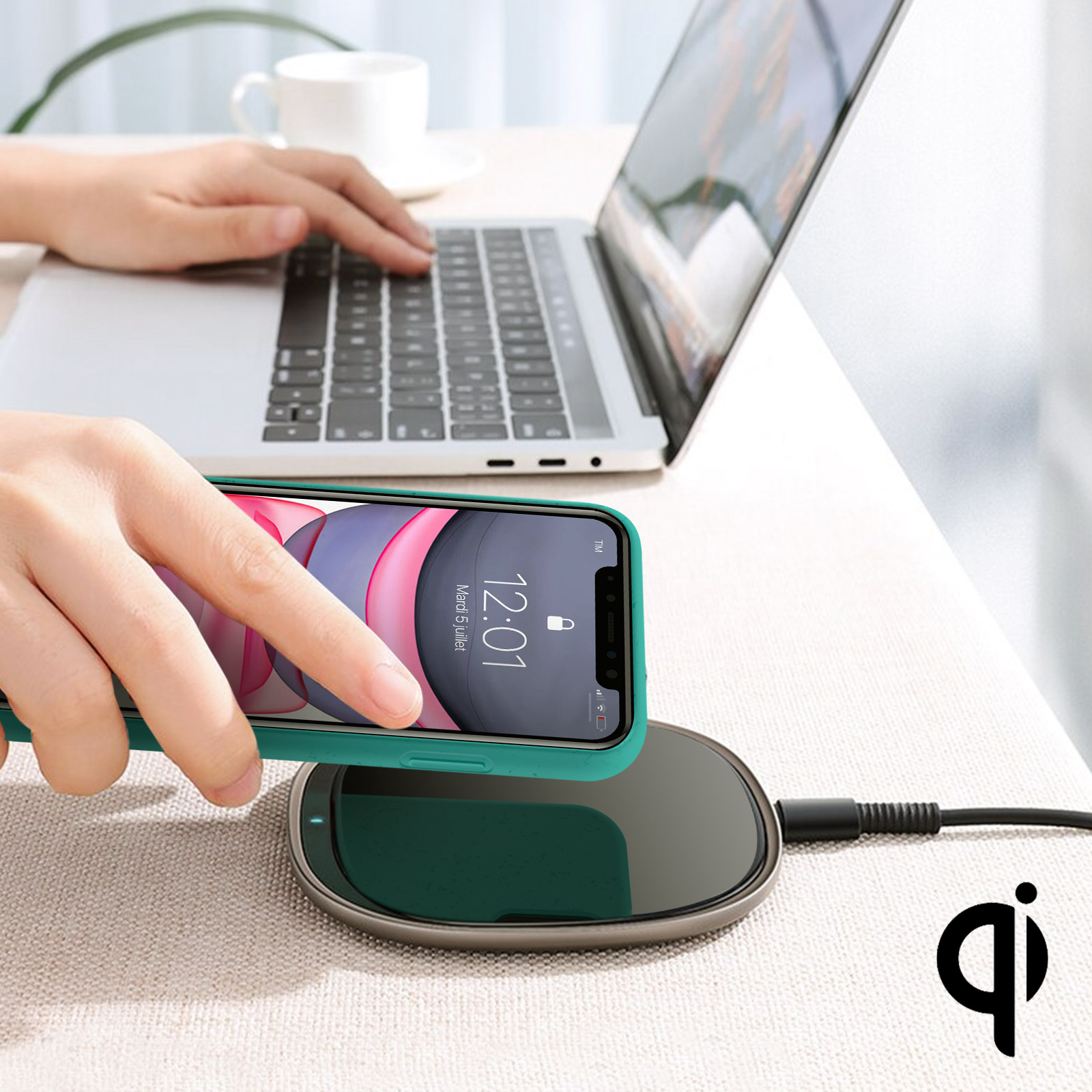 Una persona usa un laptop, con un telefono in carica su un caricatore wireless. Il telefono è verde.