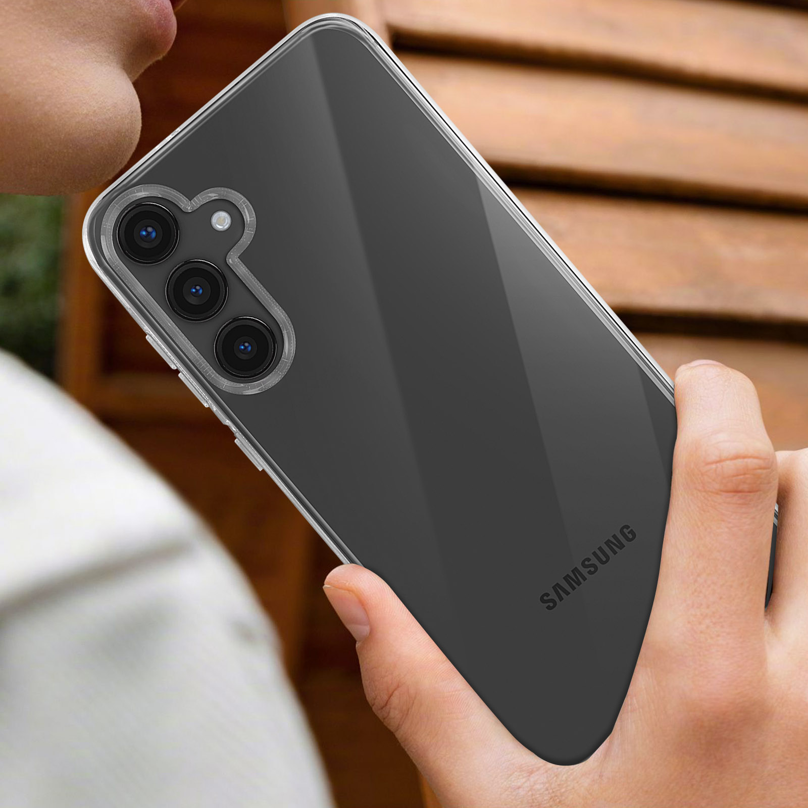 Mano che tiene un telefono con custodia trasparente. Il telefono è scuro, con il logo SAMSUNG visibile.