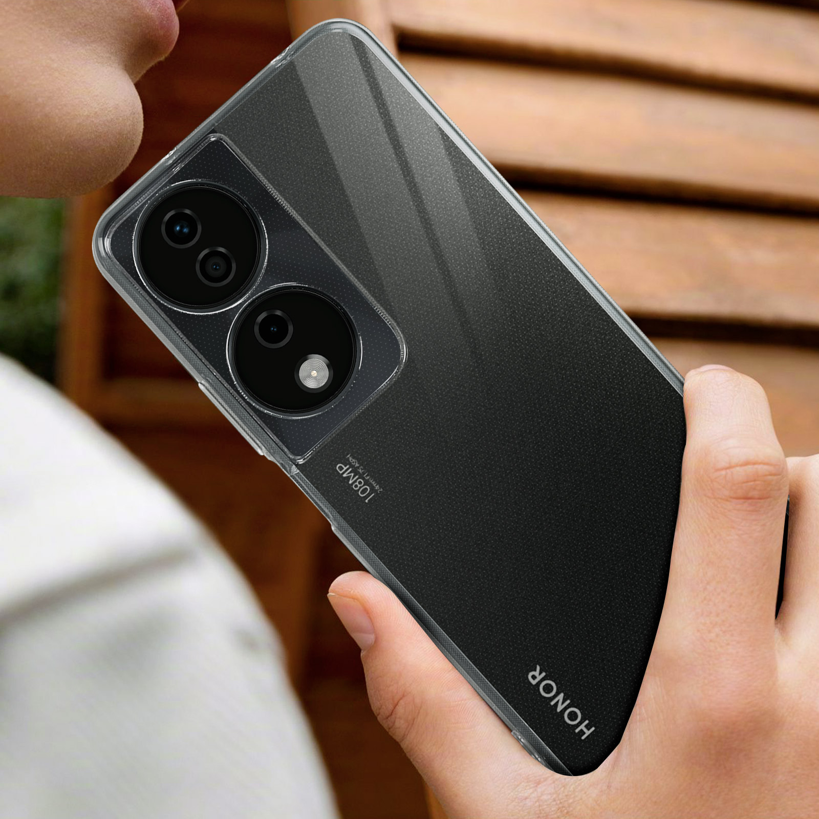 Una persona tiene in mano un telefono con una custodia trasparente. Il telefono ha il retro nero e una configurazione a doppia fotocamera.