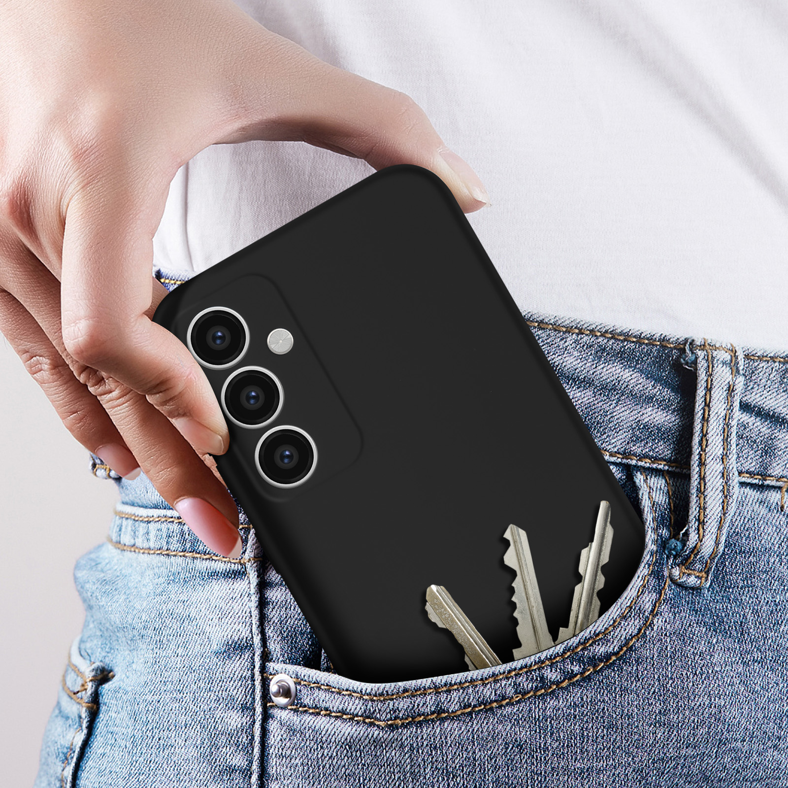 Una mano che tiene un telefono in una custodia nera in una tasca dei jeans. Chiavi anche nella tasca.