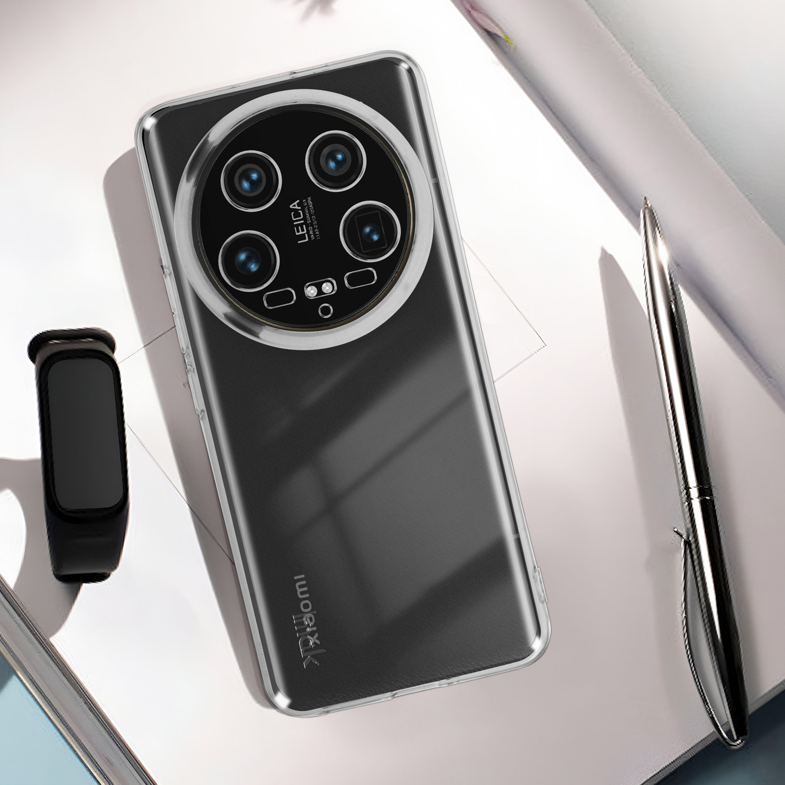 Custodia trasparente con telefono all'interno. Modulo fotocamera nero. Smartwatch e penna sullo sfondo.