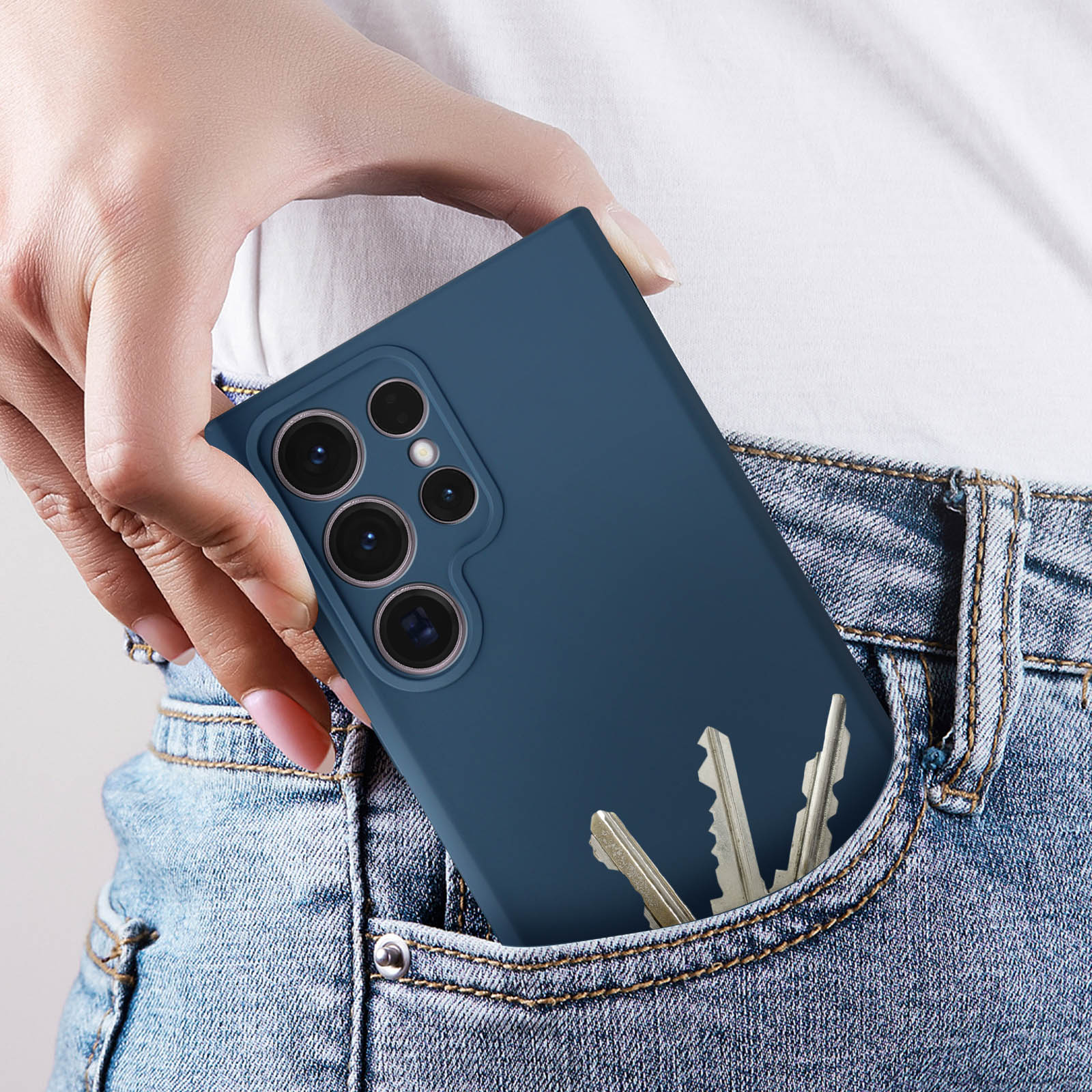 Un telefono in una custodia blu è parzialmente in una tasca di jeans, con chiavi nella stessa tasca.