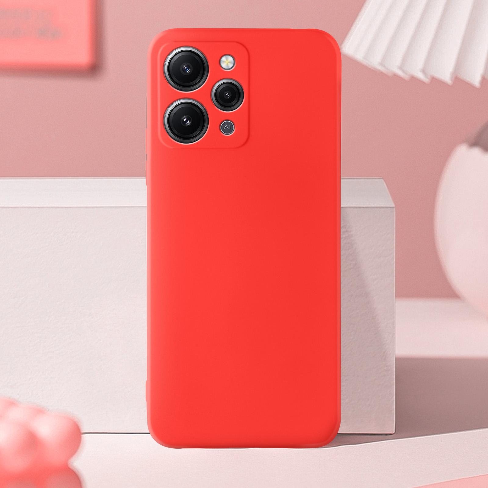 Una custodia per telefono rossa con tre fotocamere, su una scatola bianca e sfondo rosa.