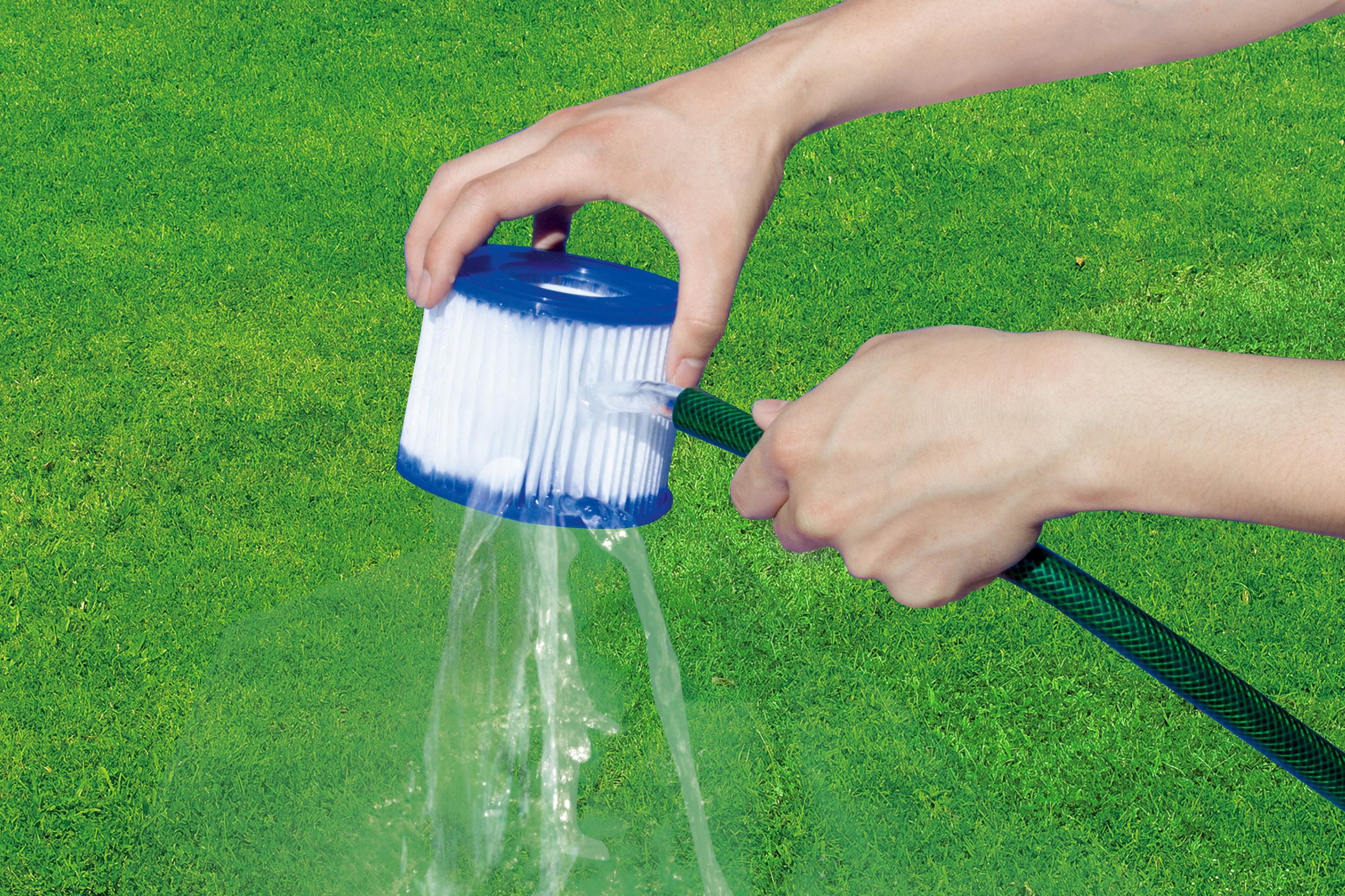 Manos limpiando un filtro con agua de una manguera verde. Fondo de hierba verde.