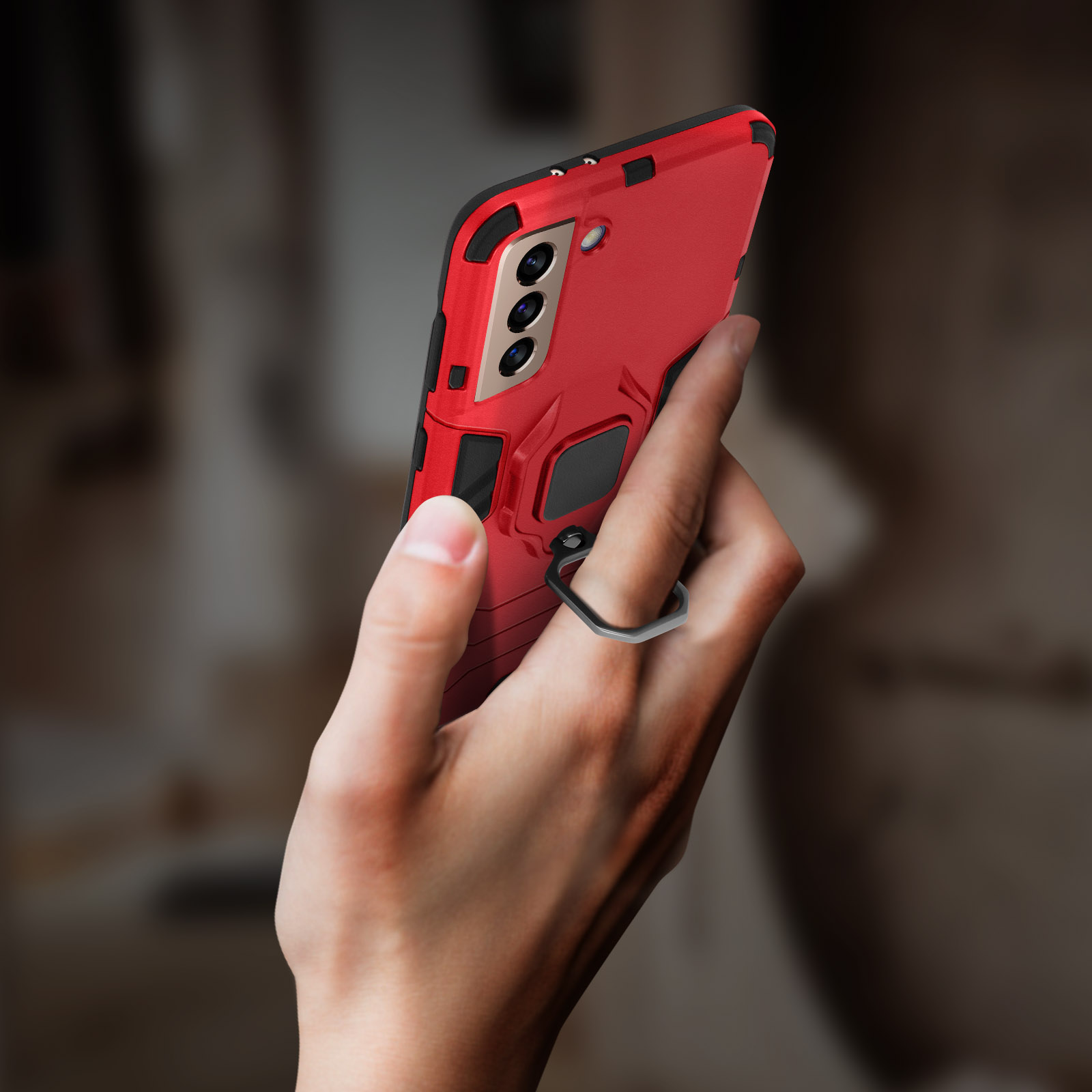 Una mano tiene un telefono rosso in una custodia protettiva con anello. Sfondo sfocato.