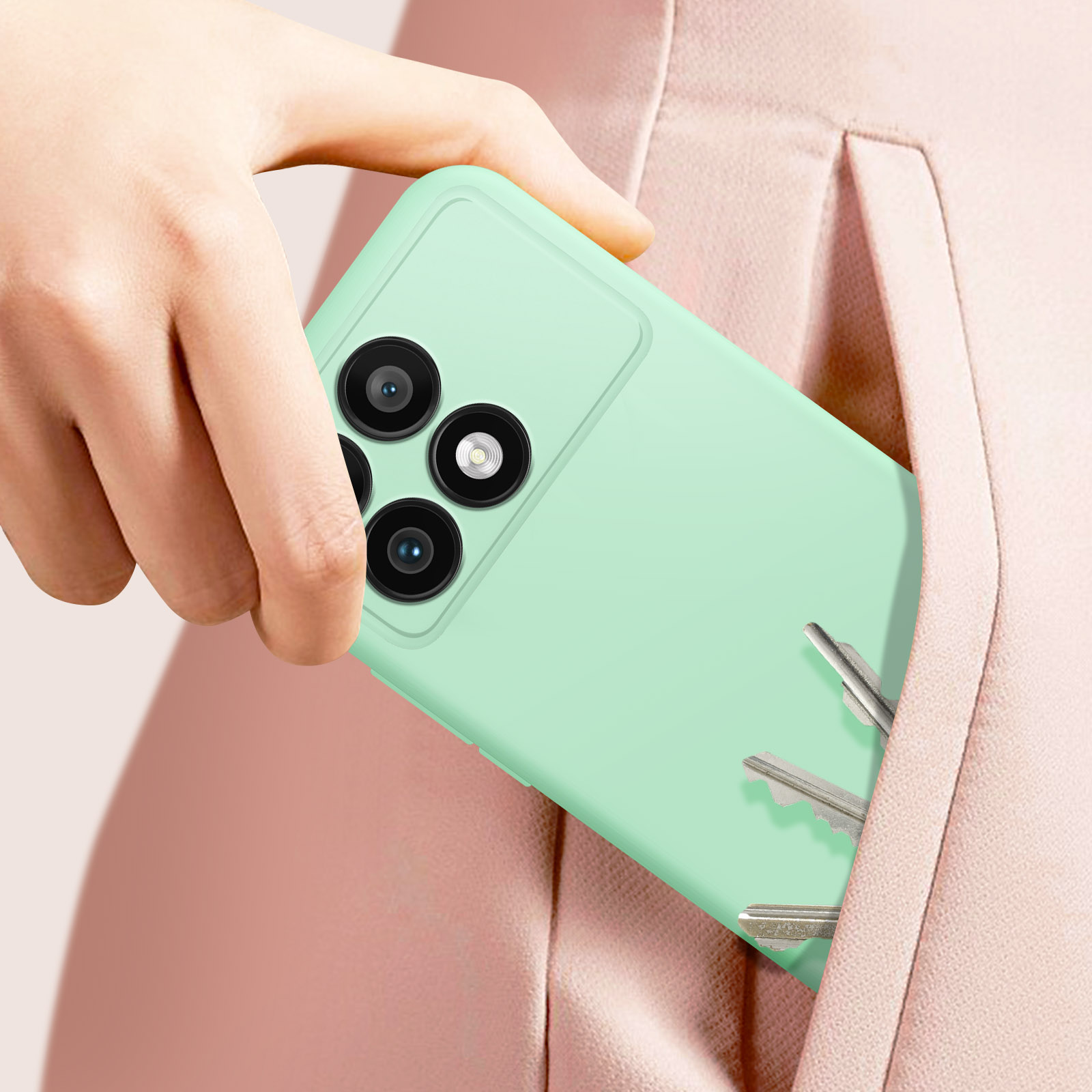 Una mano che tiene un telefono alla menta con una custodia. Le chiavi sono visibili nella tasca. Sfondo rosa.