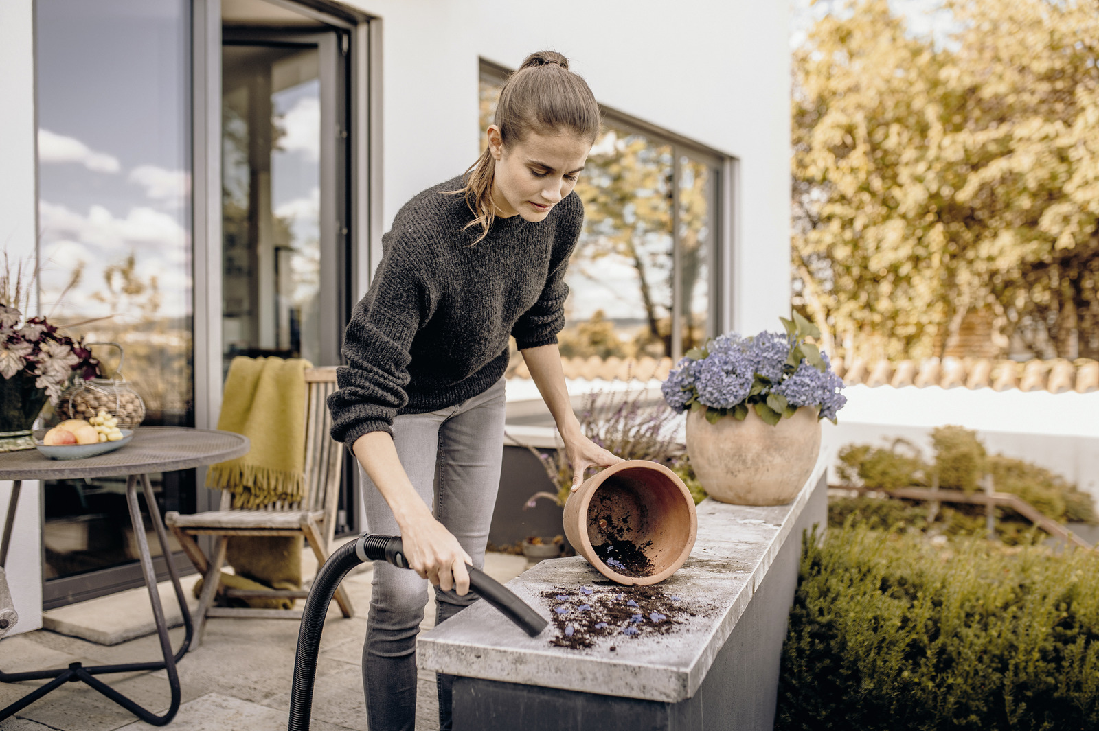 Eine Frau reinigt einen Blumentopf auf einer Terrasse mit einem Staubsauger.