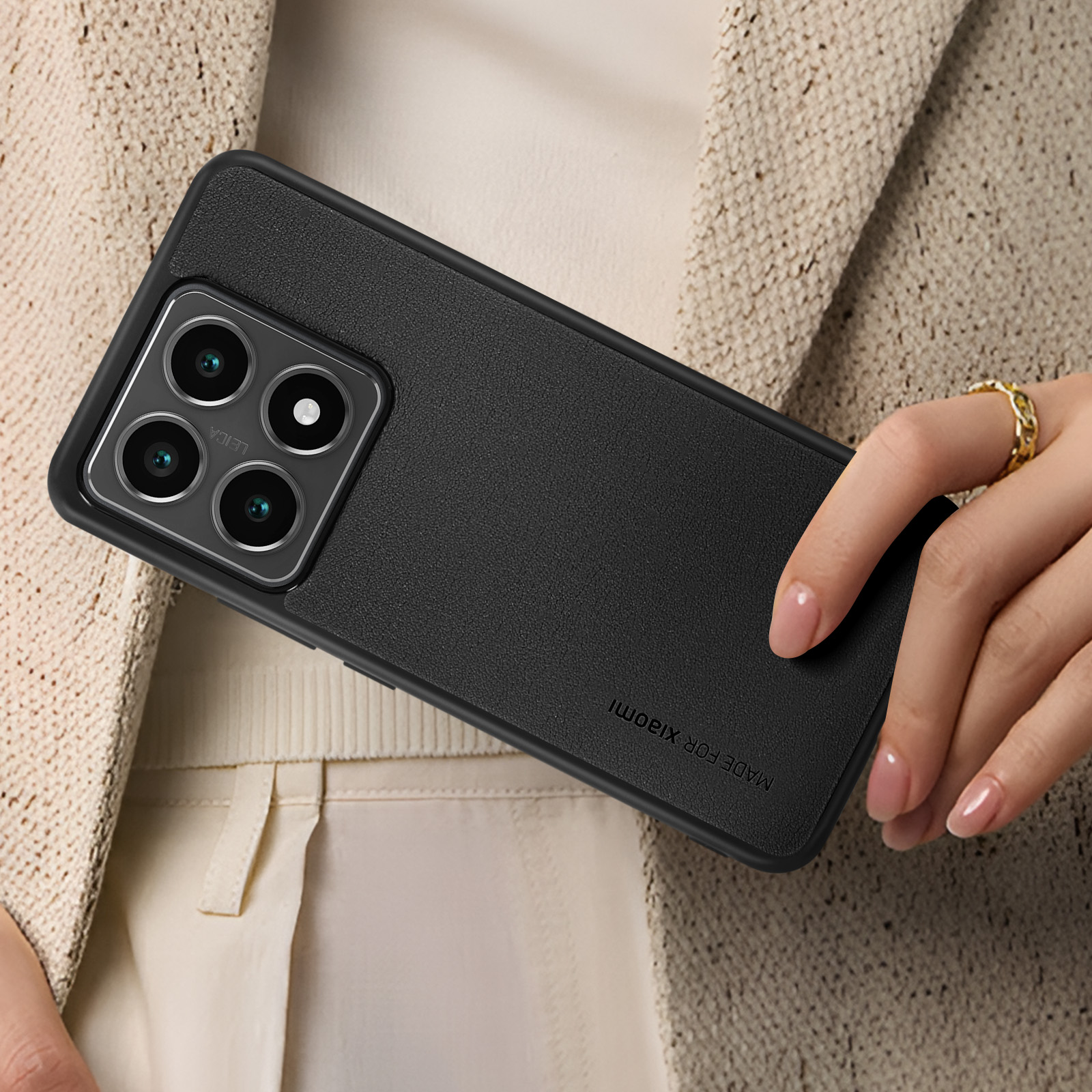 Coque de téléphone noire avec quatre objectifs. Le téléphone est tenu par une main. Fond beige.