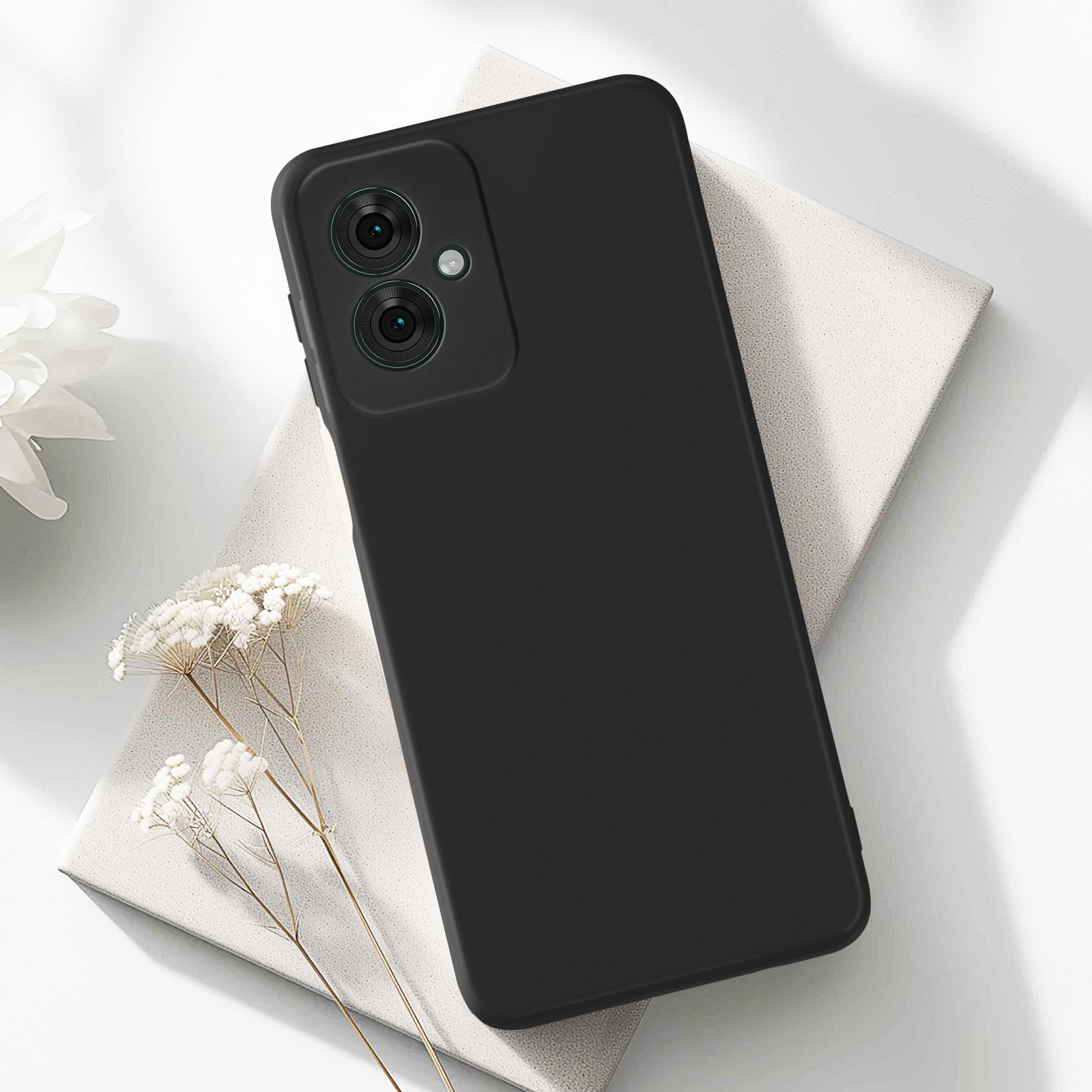 Eine schwarze Handyhülle auf weißer Oberfläche mit weißer Blume.