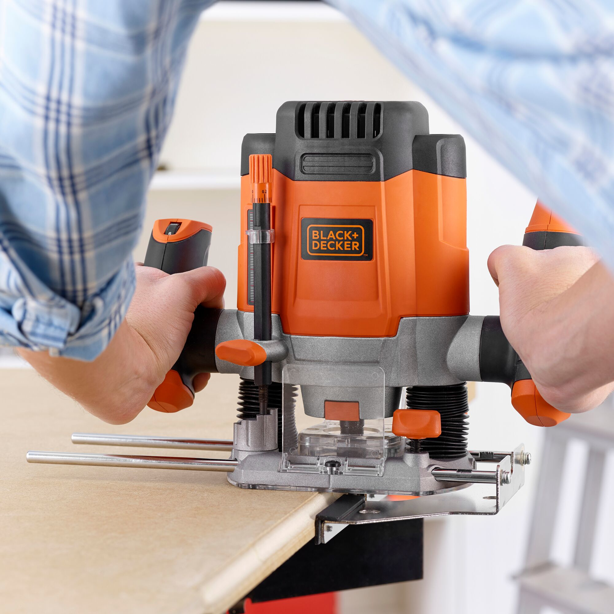 Una persona usando un router Black+Decker en una superficie de madera. El router es naranja y negro.