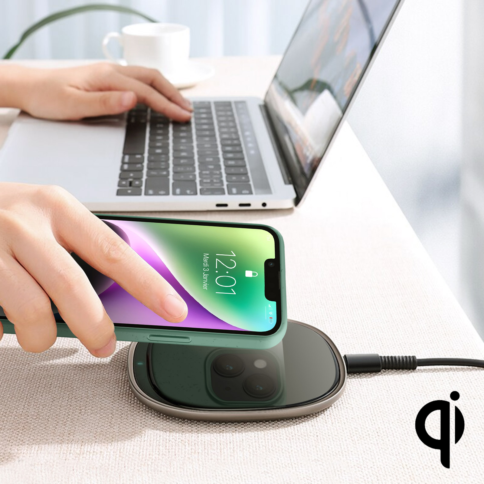 Una persona usa un laptop mentre carica un telefono in modalità wireless. Il telefono è su un caricatore nero.