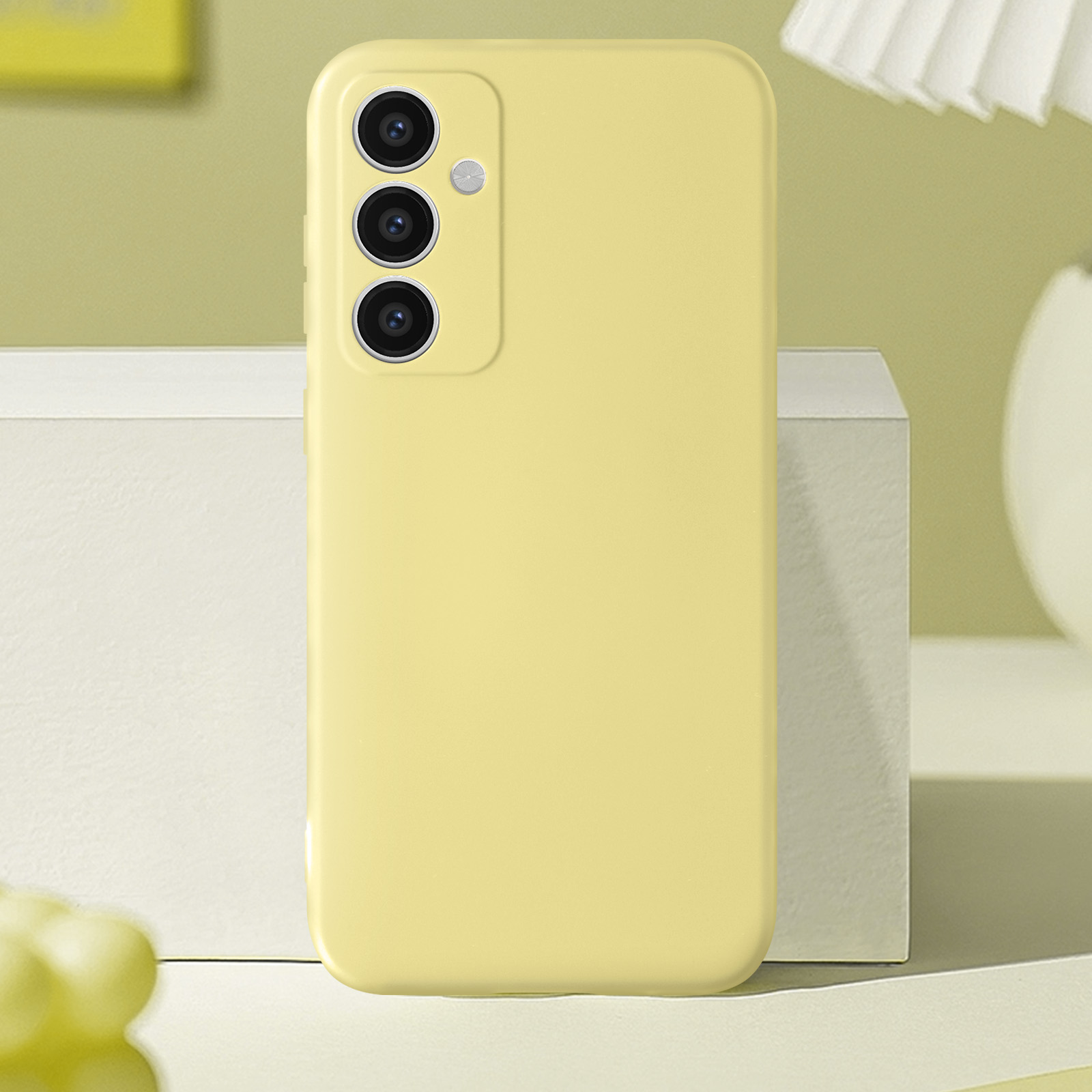 Custodia gialla con tre fotocamere posteriori, su un blocco bianco, sfondo verde chiaro.