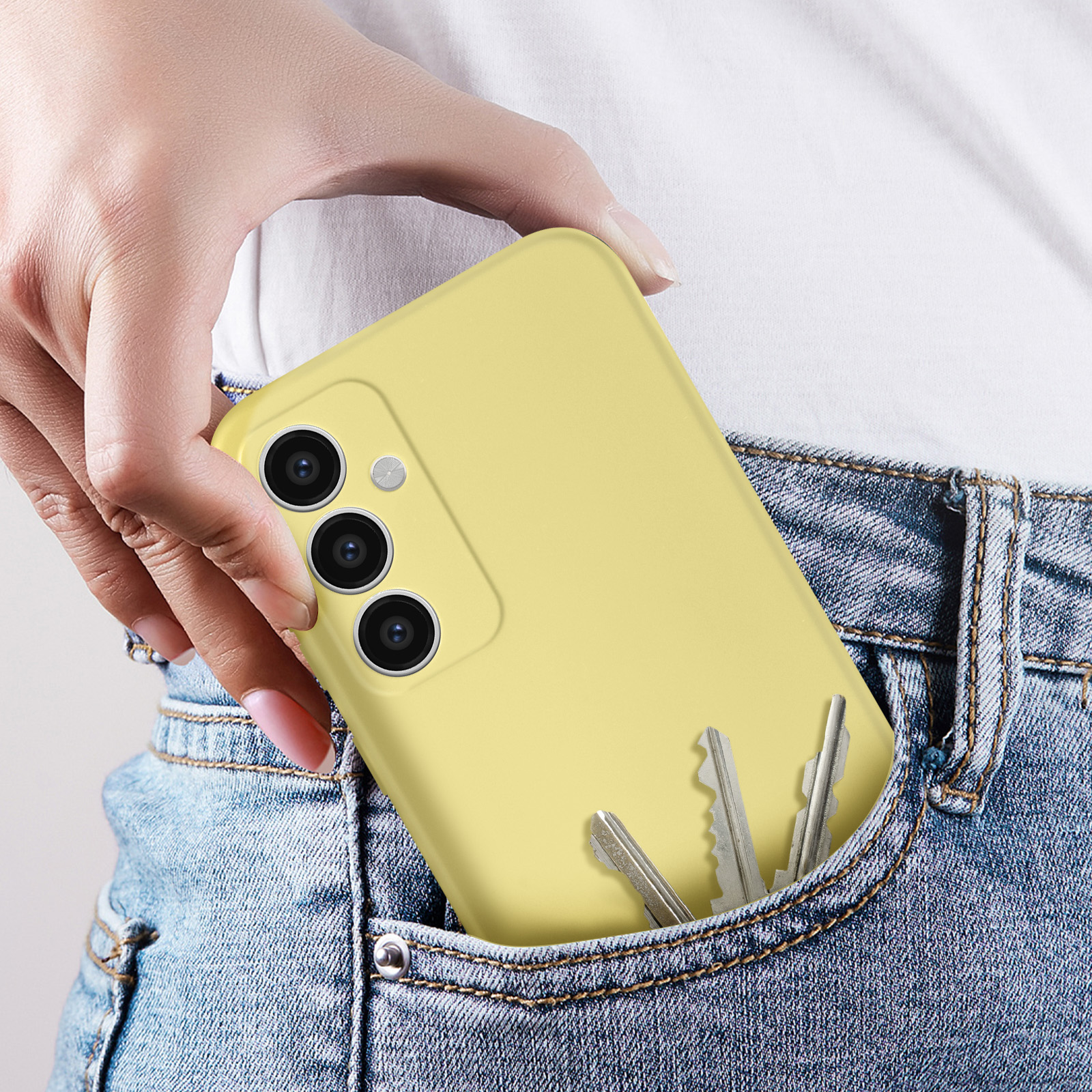Una mano che tiene un telefono giallo in una tasca con delle chiavi. Lo sfondo è un paio di jeans.