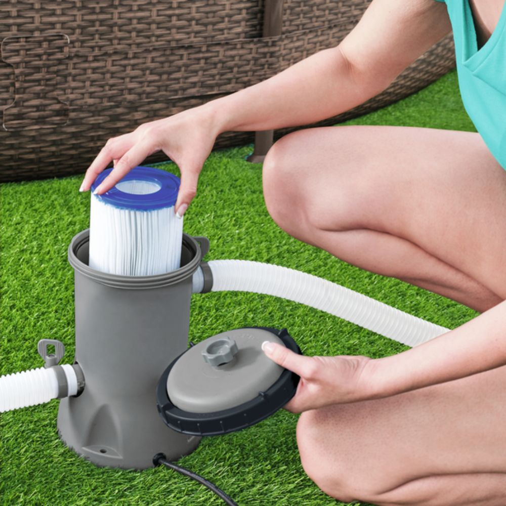 Personne installant un filtre dans une pompe de piscine grise, sur de l'herbe verte.