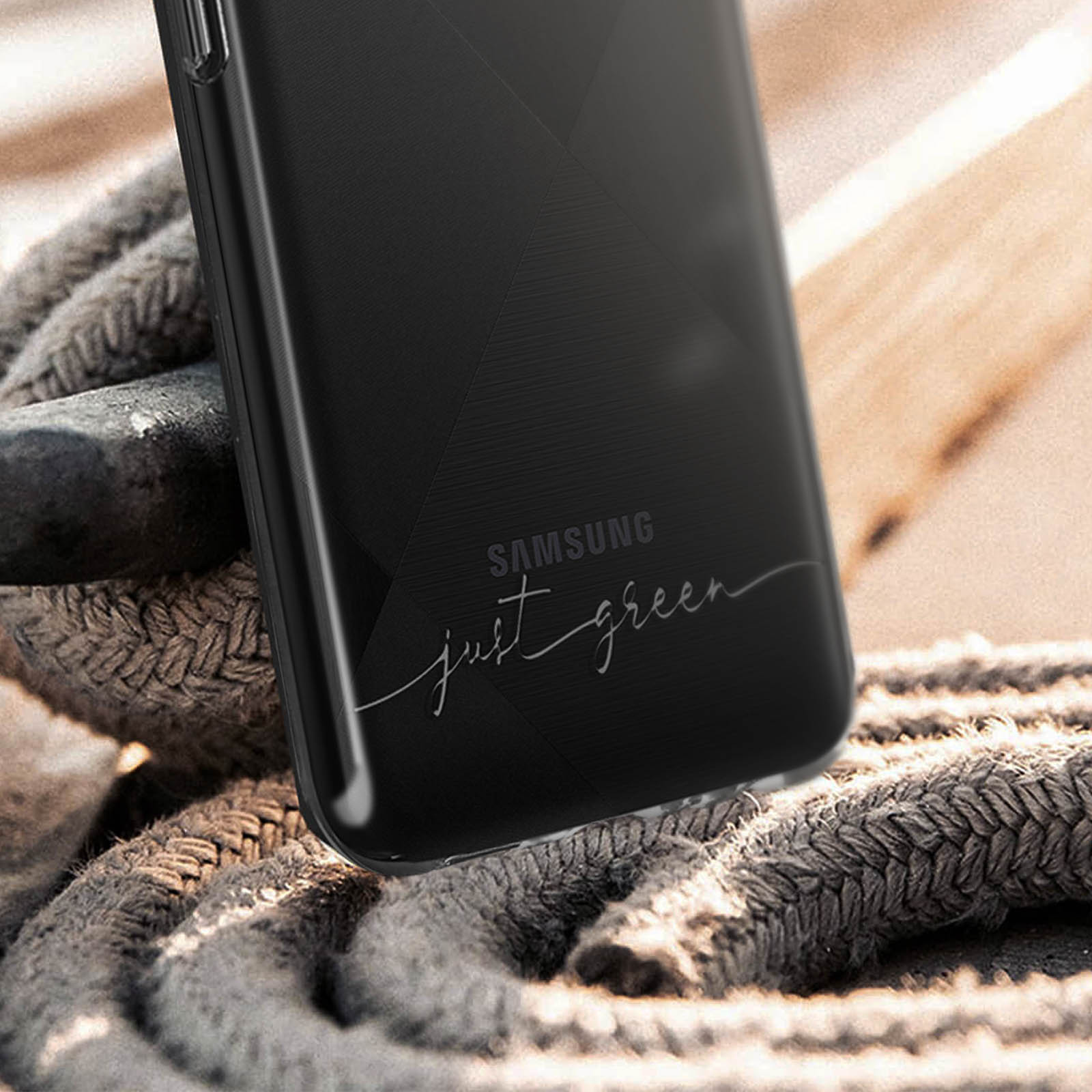 Custodia nera per telefono con 'SAMSUNG' e 'just green' stampato sopra. La custodia è su una superficie di legno.