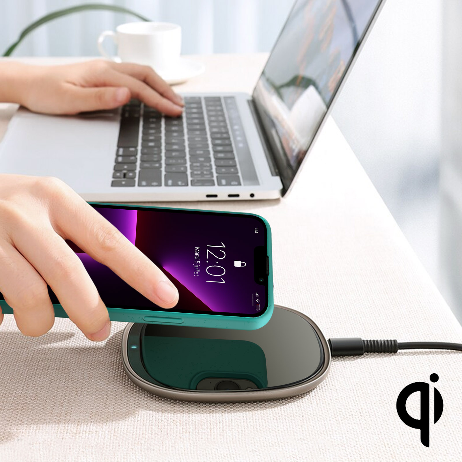 Una mano posiziona un telefono su un caricabatterie wireless accanto a un laptop.