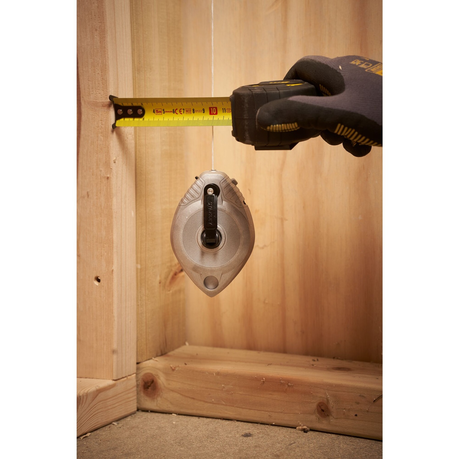 Narzędzie poziomujące mierzy drewnianą ramę za pomocą sznurka traserskiego i miarki.