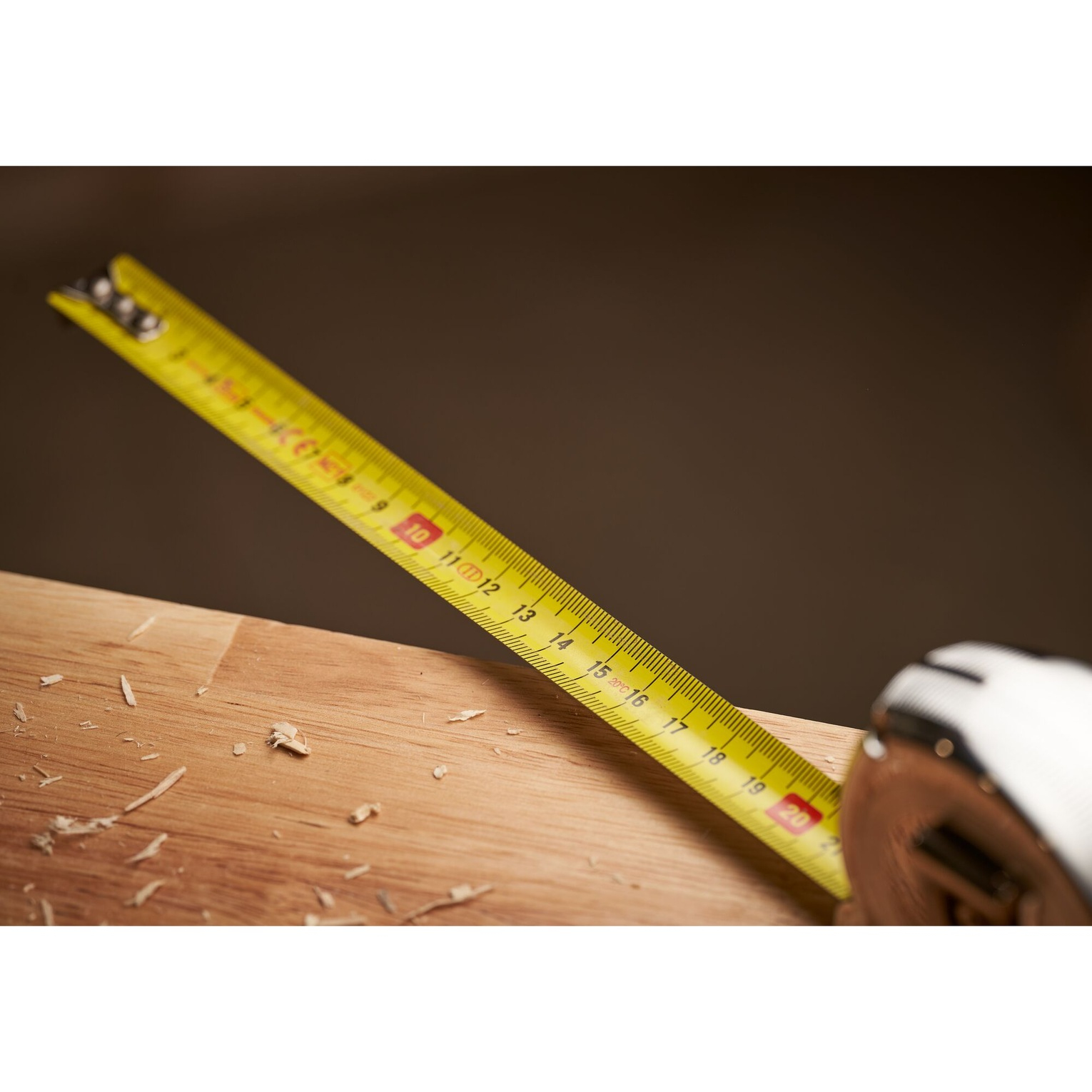 Żółta miarka rozciągnięta na drewnianej powierzchni z wiórami.