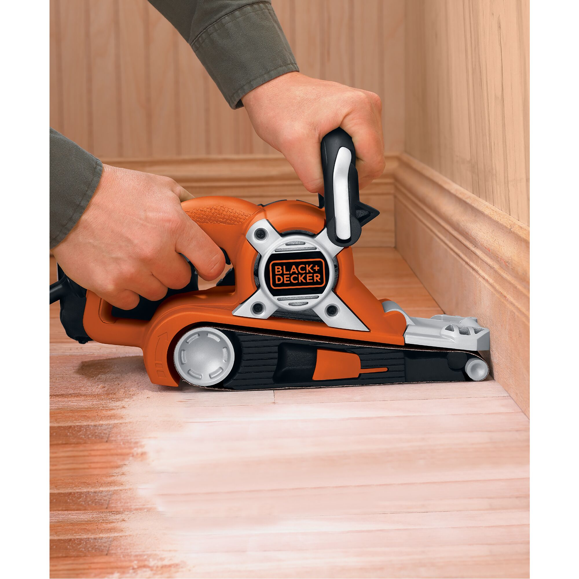 Hände halten einen orange-schwarzen Schleifer auf einem Holzboden. Der Boden ist teilweise geschliffen.