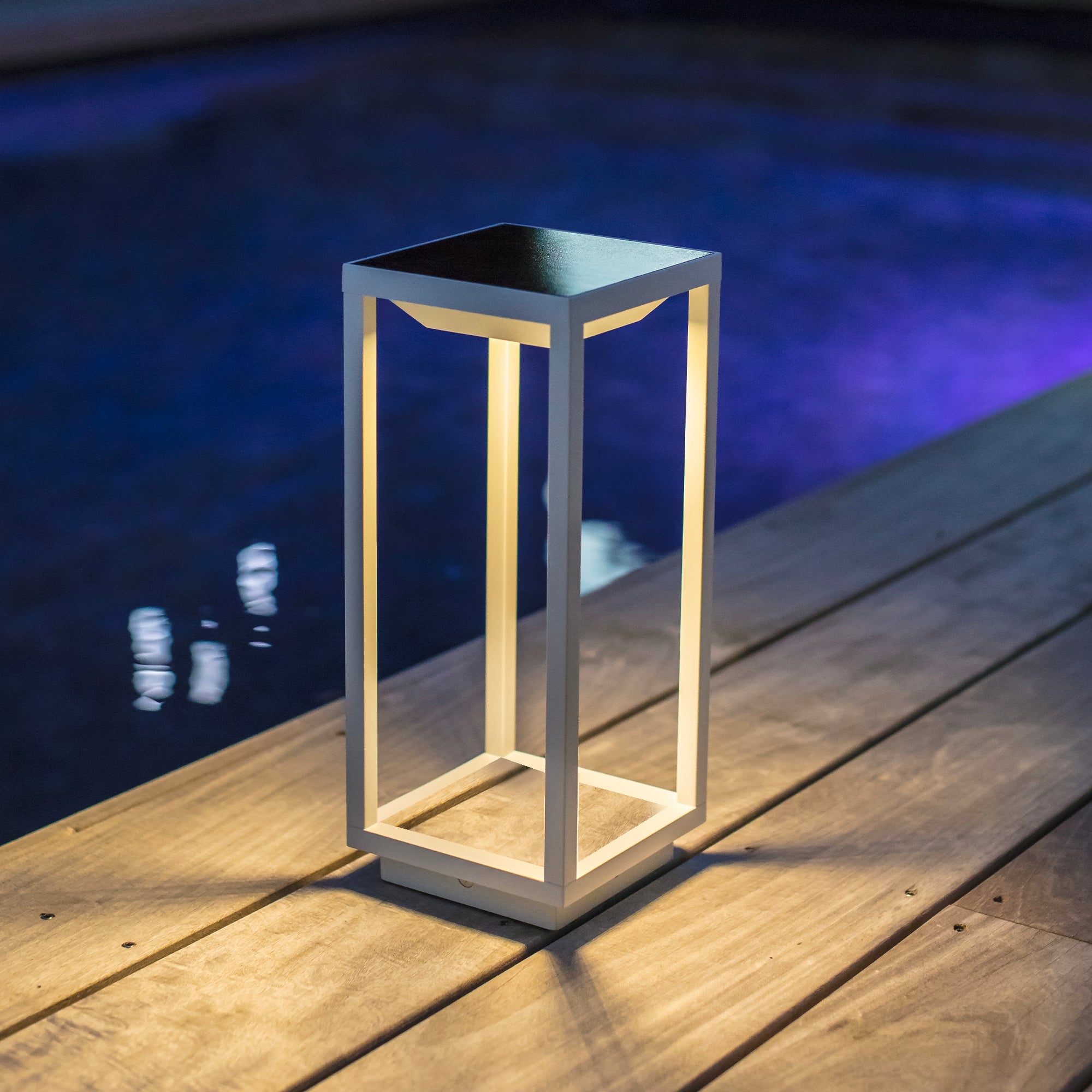 Weiße quadratische Außenlampe mit klarem Licht. Sie steht auf einem Holzdeck.