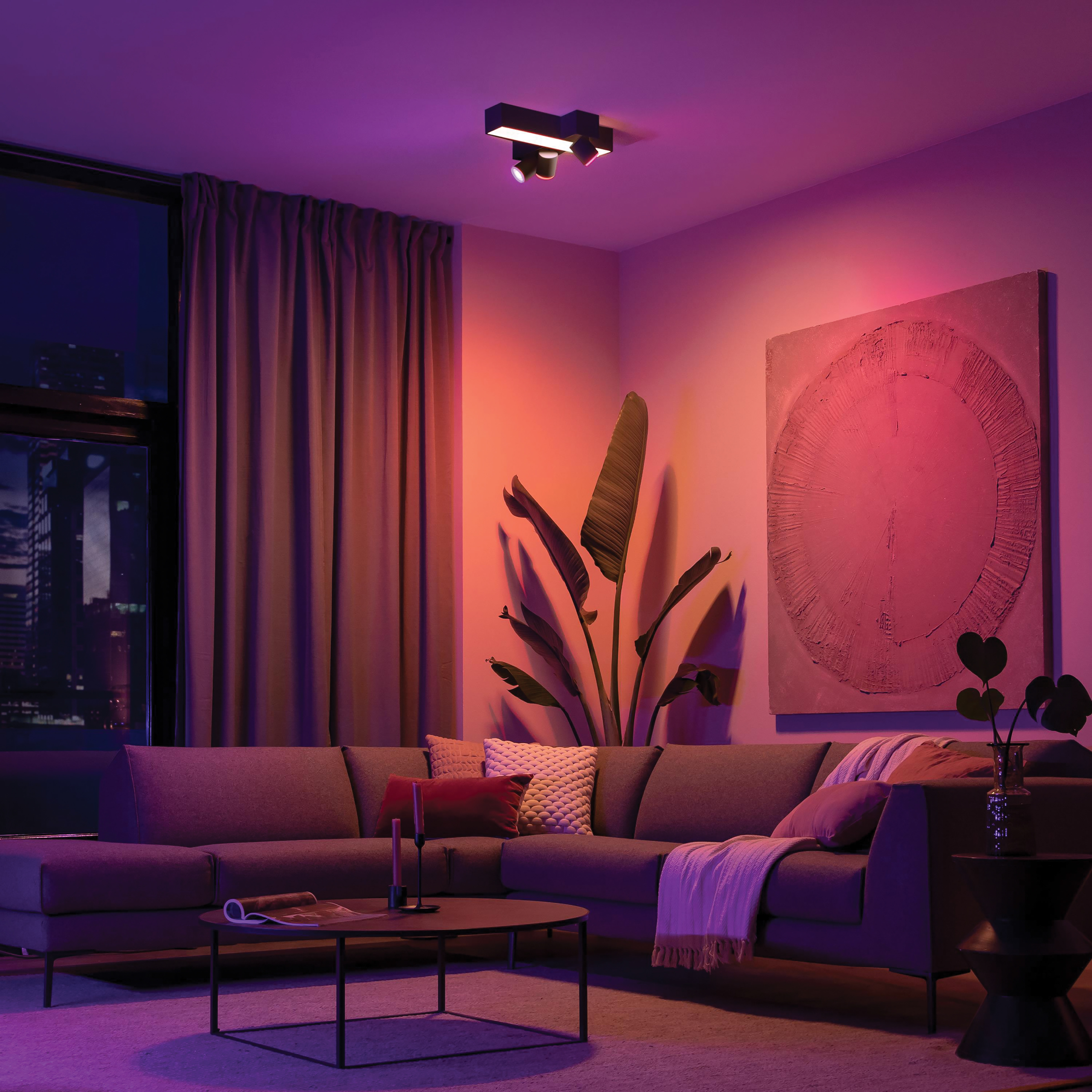 Een moderne woonkamer verlicht met gekleurde lichten van plafondarmaturen, met een bank en kunstwerken.
