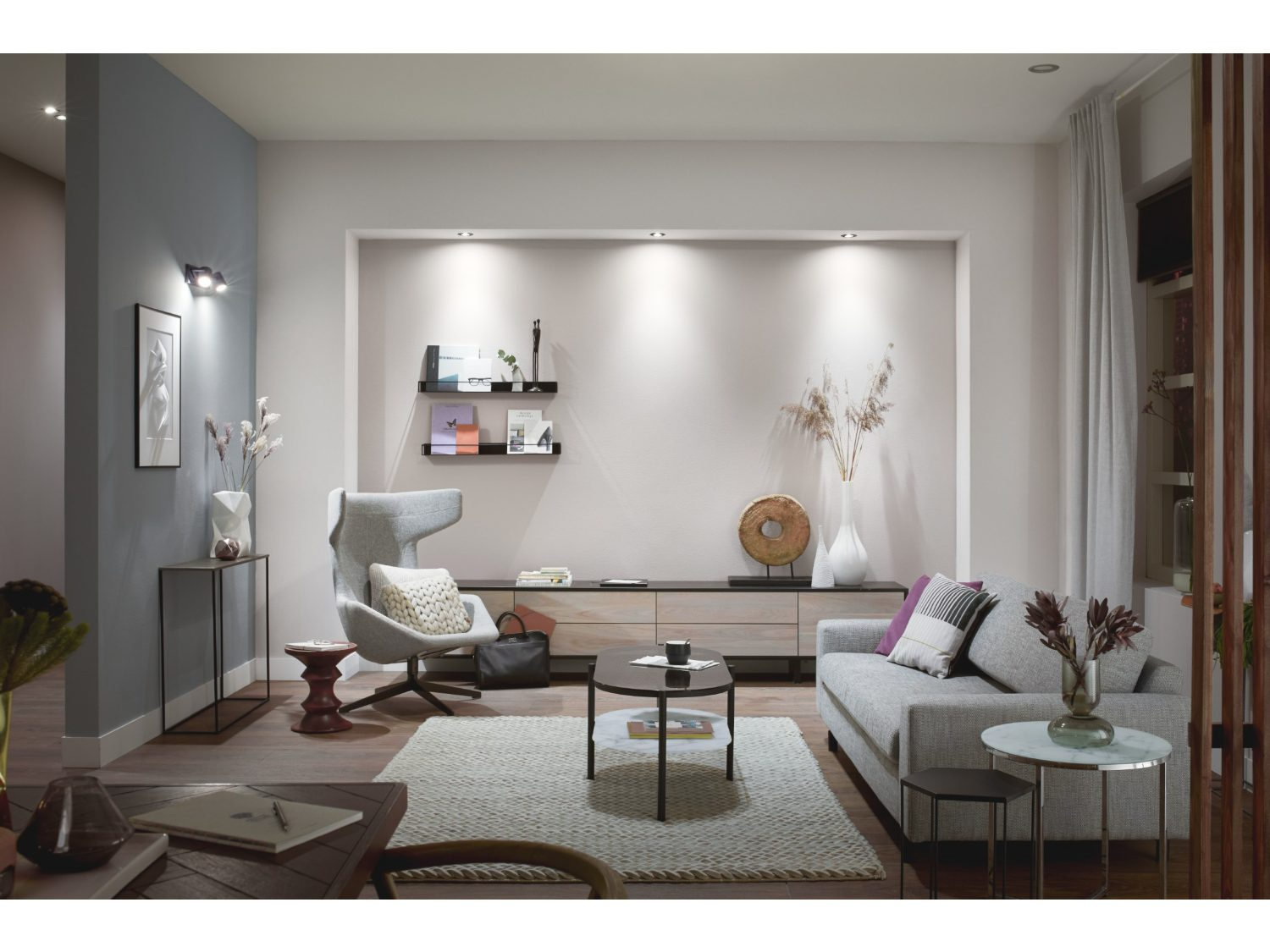 Salon z kanapą, krzesłem, stołami, lampami i dekoracjami. Neutralne kolory.