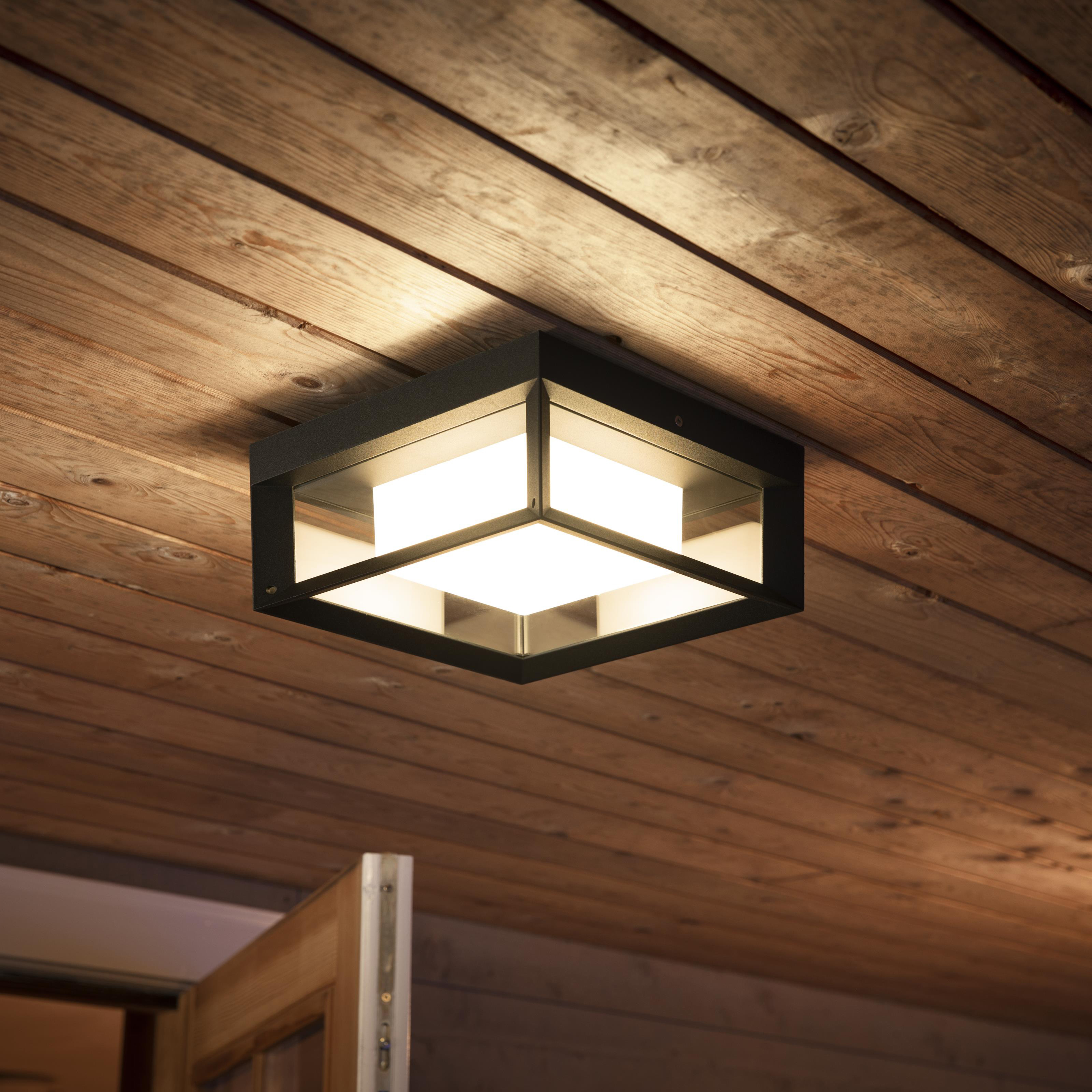 Kwadratowa oprawa oświetleniowa sufitowa z czarną ramą, zamontowana na drewnianym suficie.