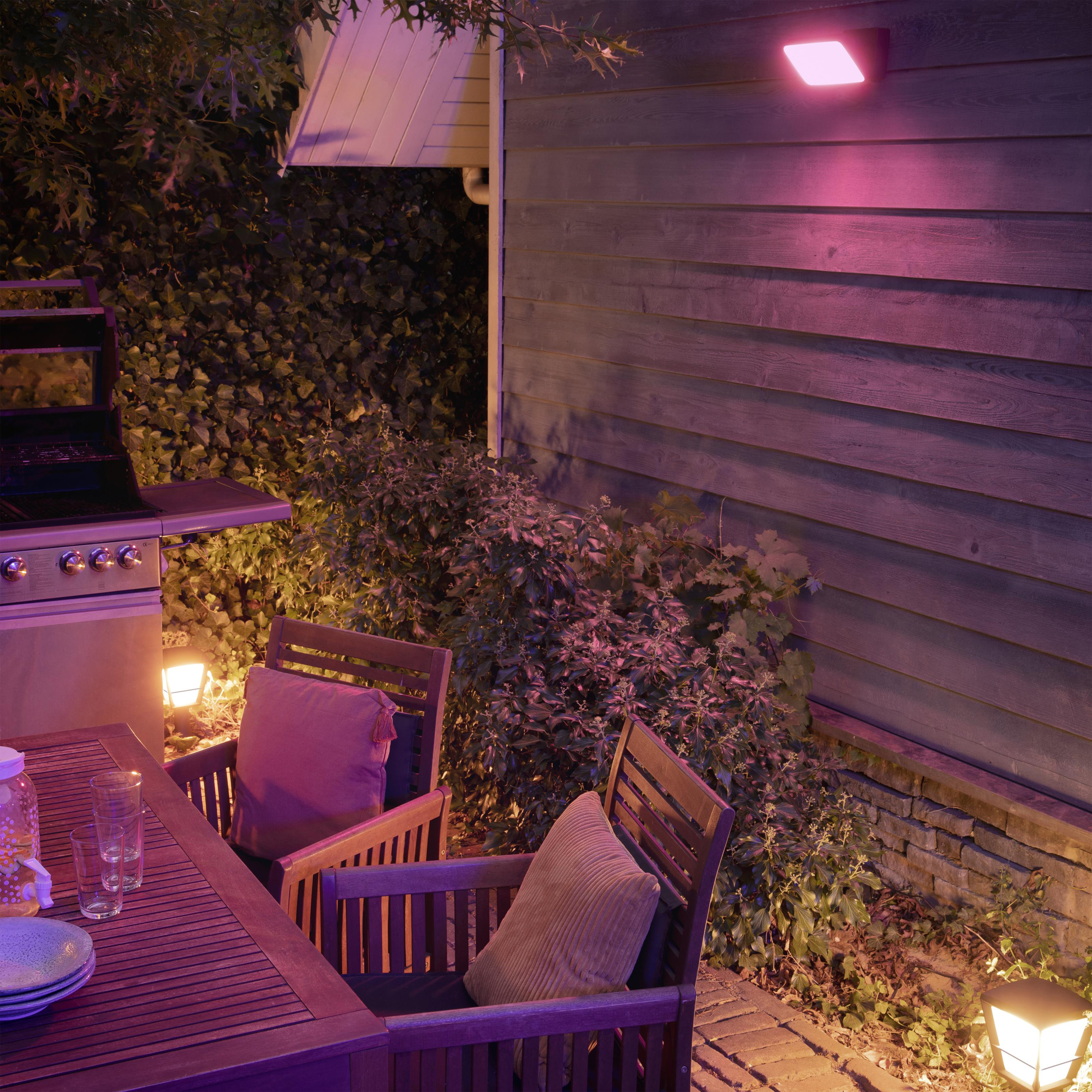 Scène extérieure avec barbecue, table, chaises et mur éclairé en rose la nuit.