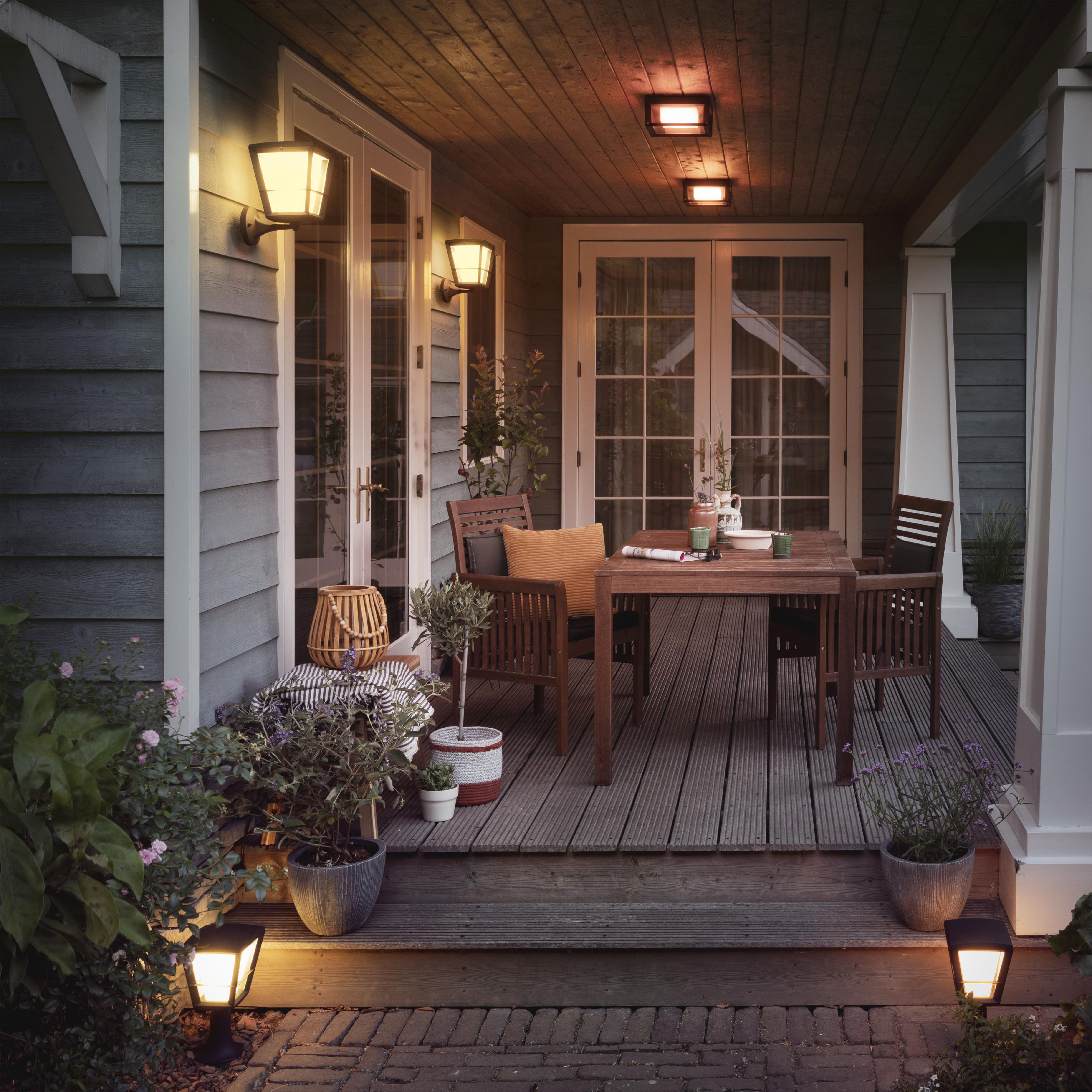 Vue extérieure d'un porche avec lumières, table et plantes.