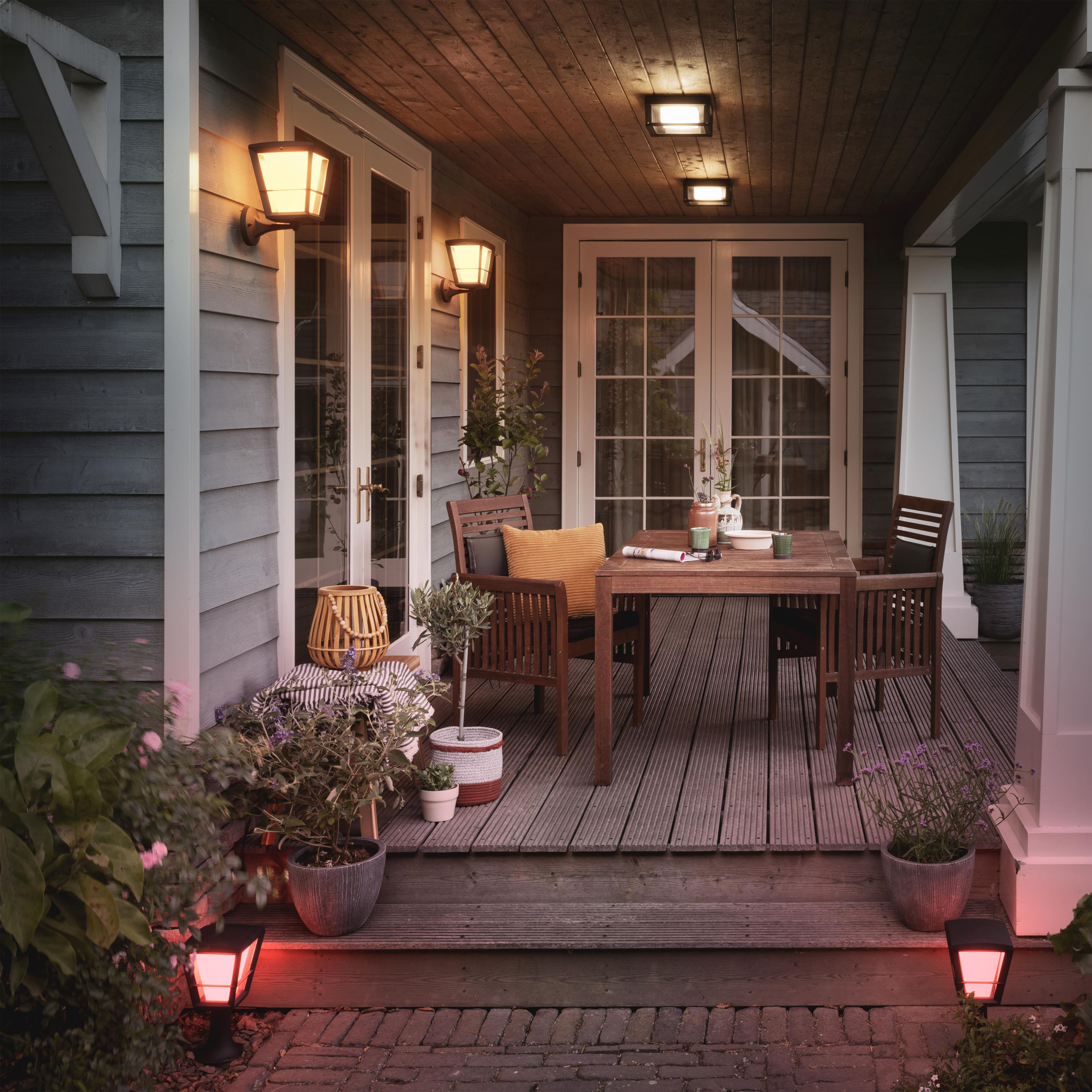 Un porche bien éclairé avec des meubles et des lumières d'extérieur. Il y a des plantes en pot et un plancher en bois.