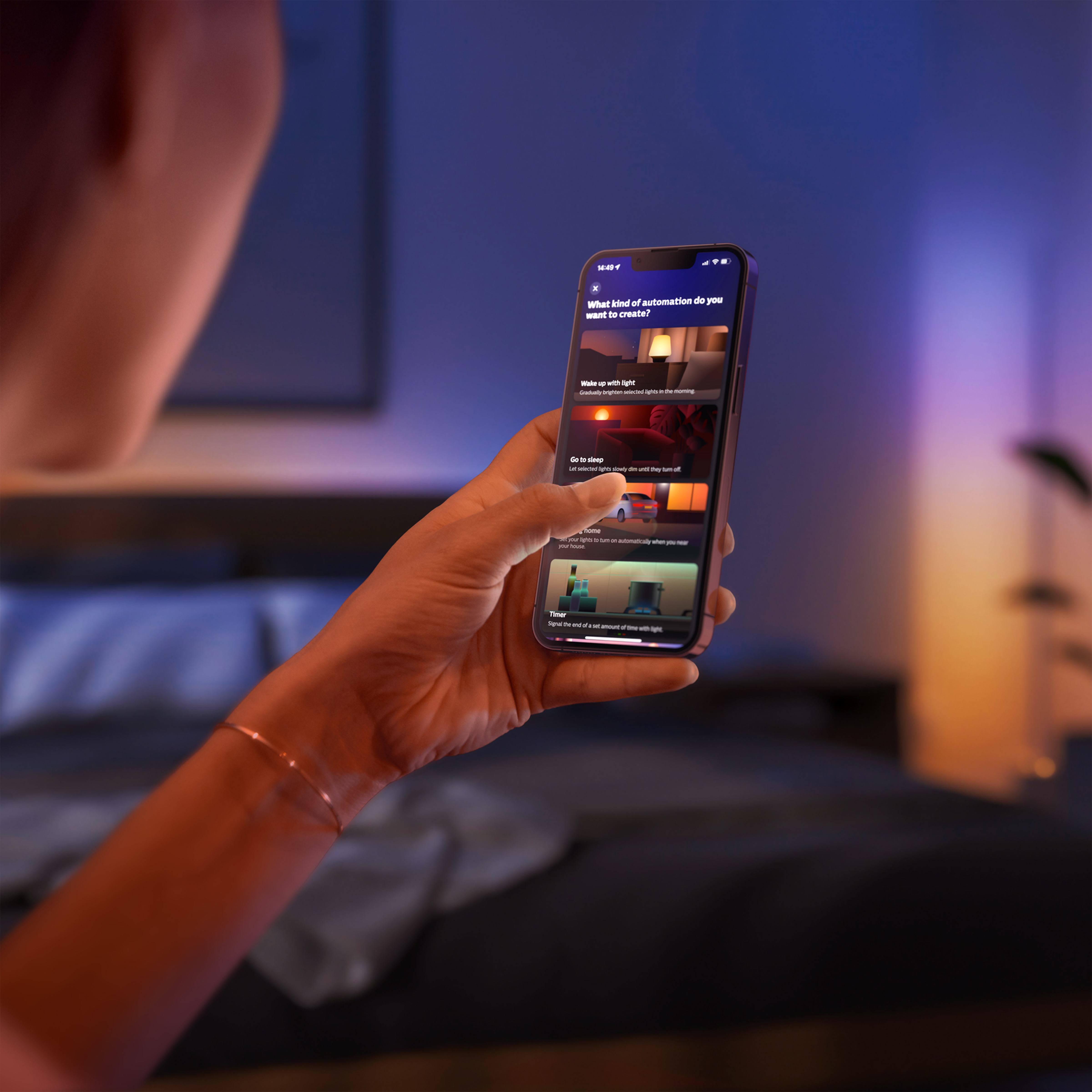 Osoba trzymająca telefon z aplikacją inteligentnego domu na łóżku, z miękkim światłem.
