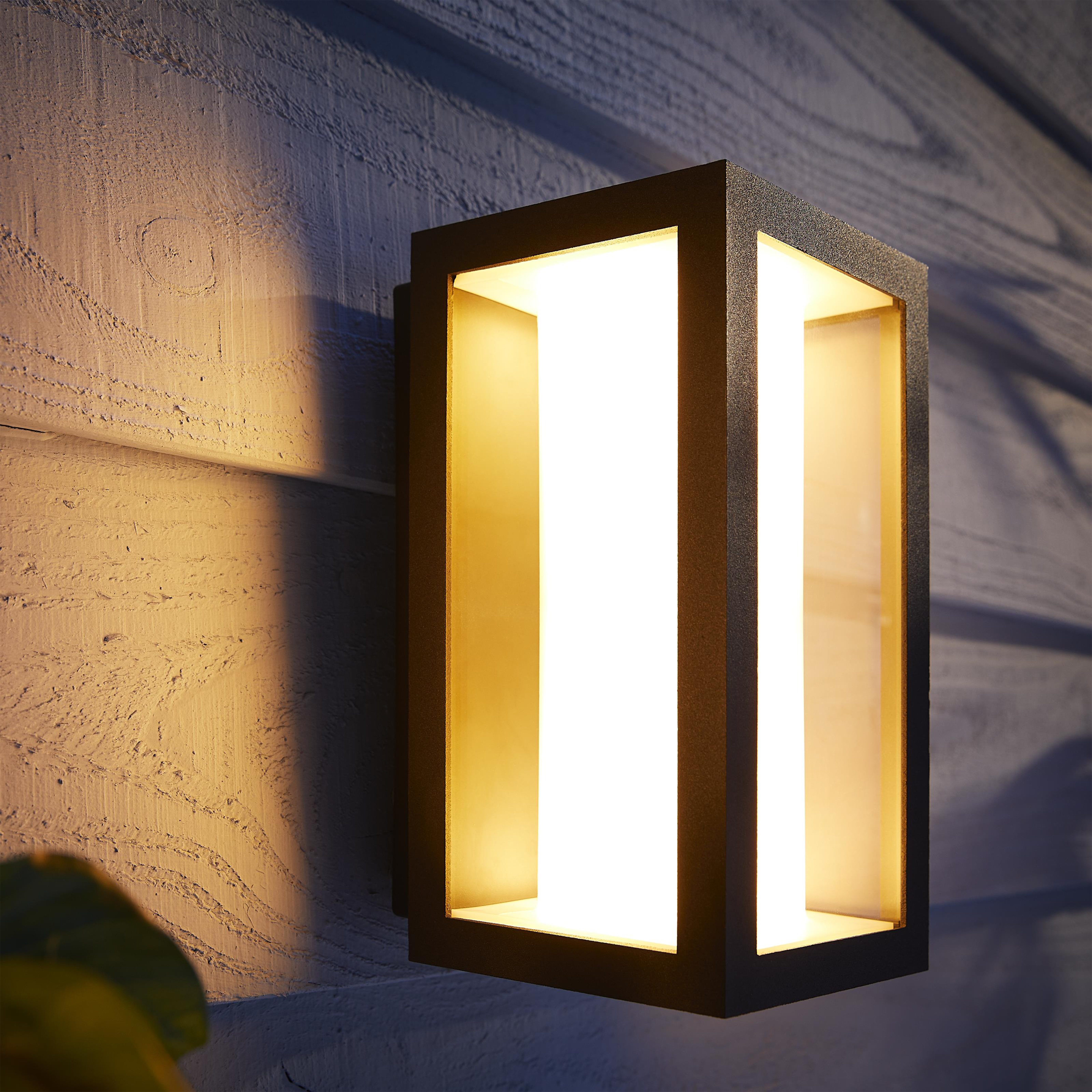 Schwarze rechteckige Außenwandleuchte, beleuchtet, auf Holzverkleidung.