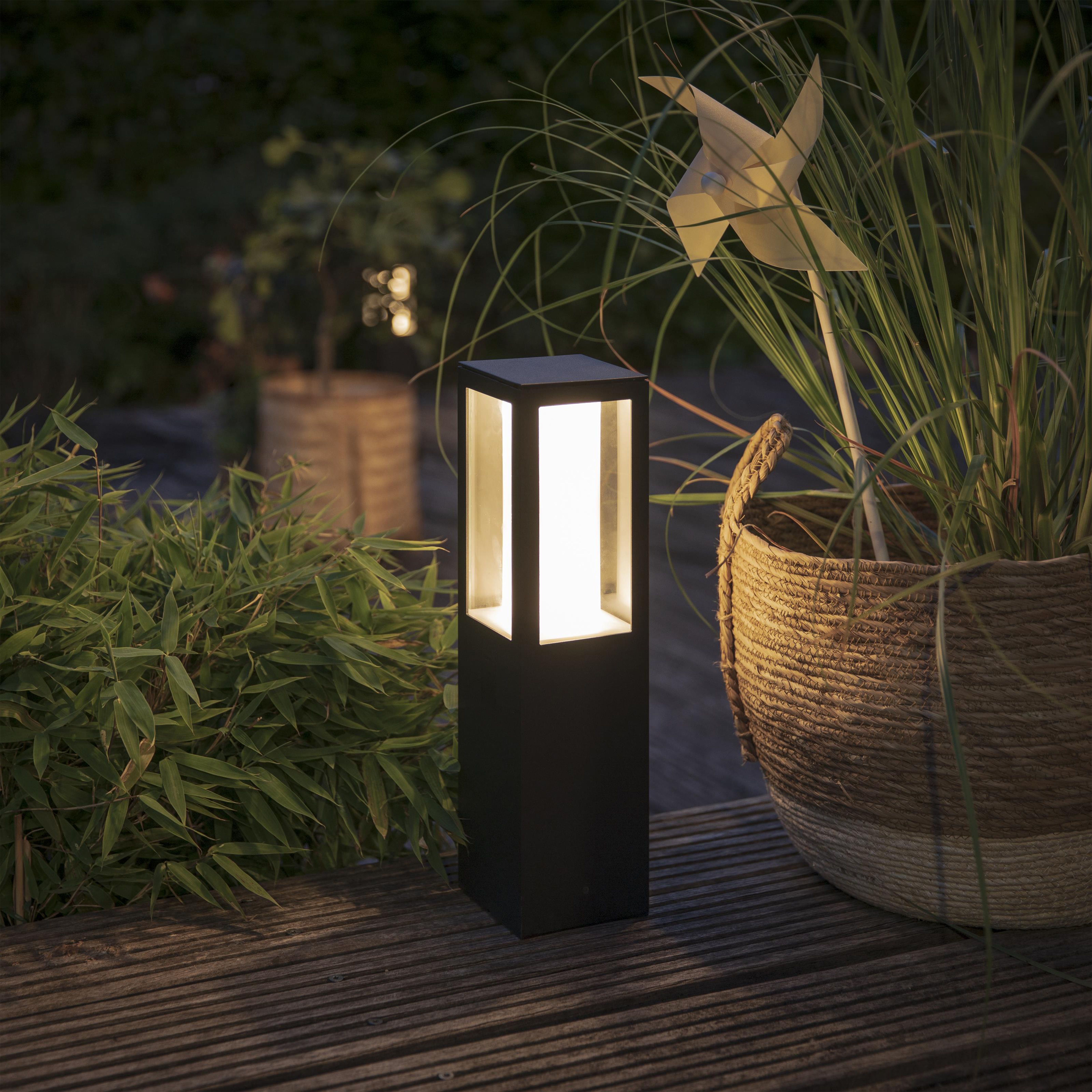 Czarna lampa zewnętrzna ze światłem i rośliną w koszu na drewnianym tarasie.