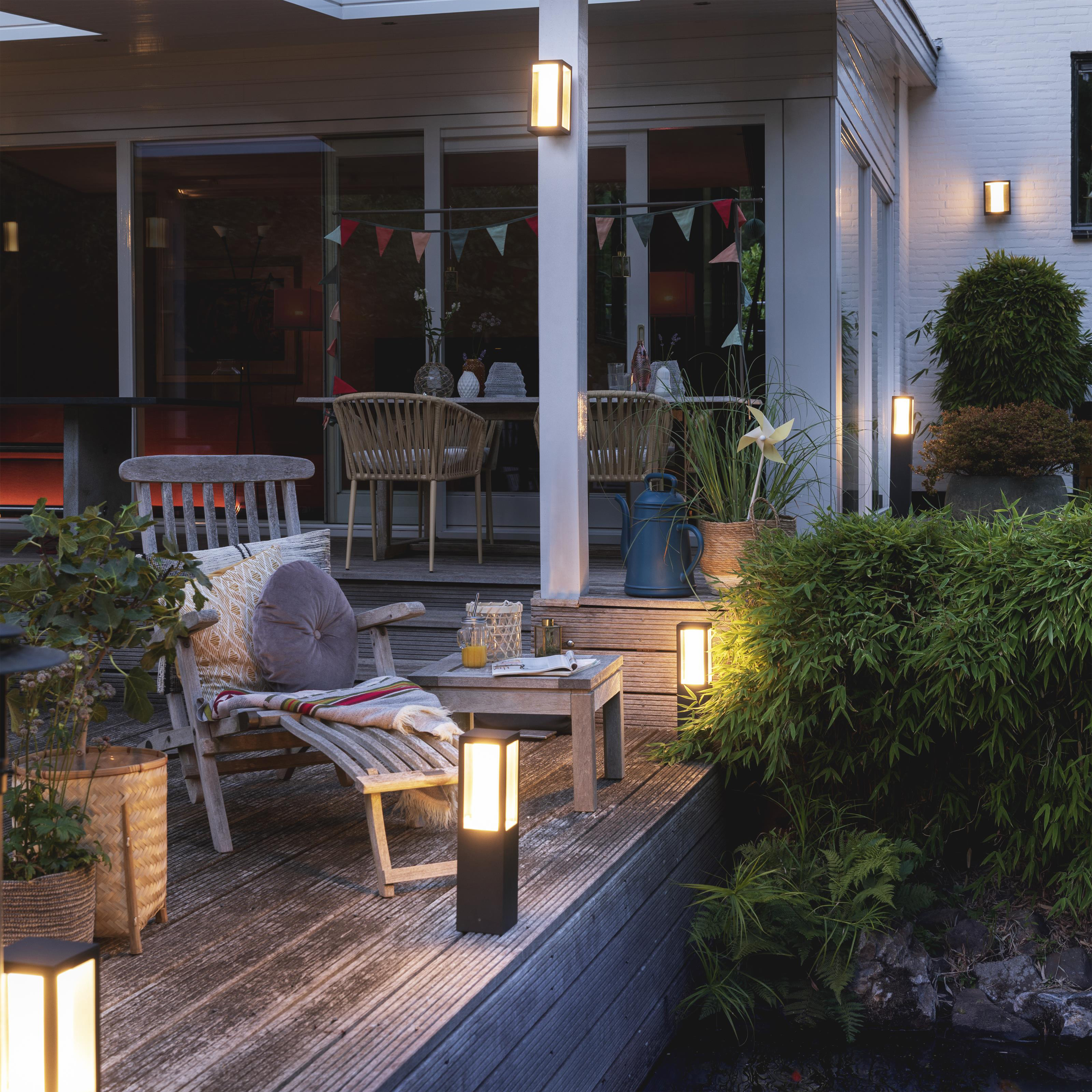 Scena na zewnątrz z oświetleniem na tarasie. Na zdjęciu drewniane meble i rośliny.