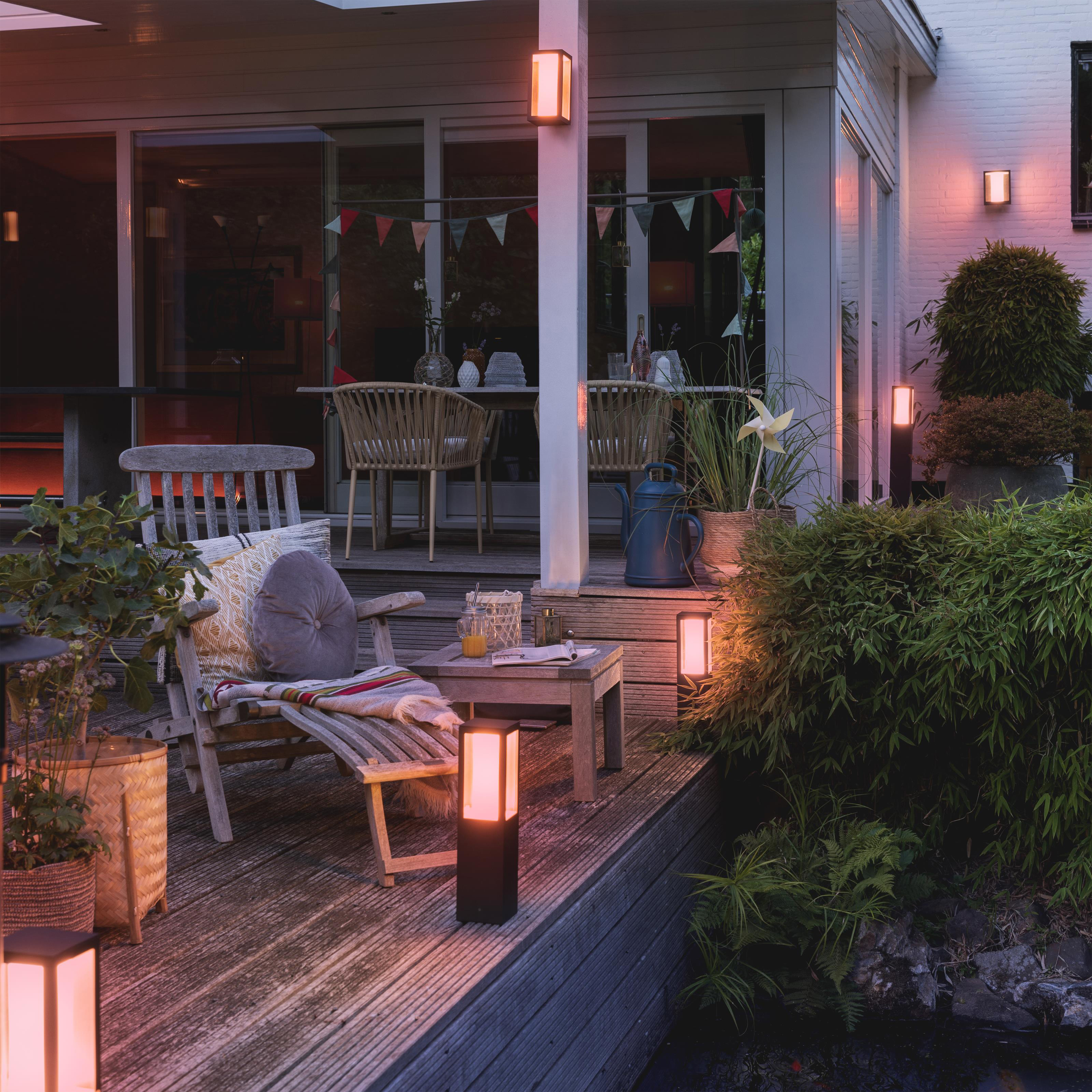 Scena na patio na zewnątrz z oświetleniem, stołem, roślinami i miejscami do siedzenia.