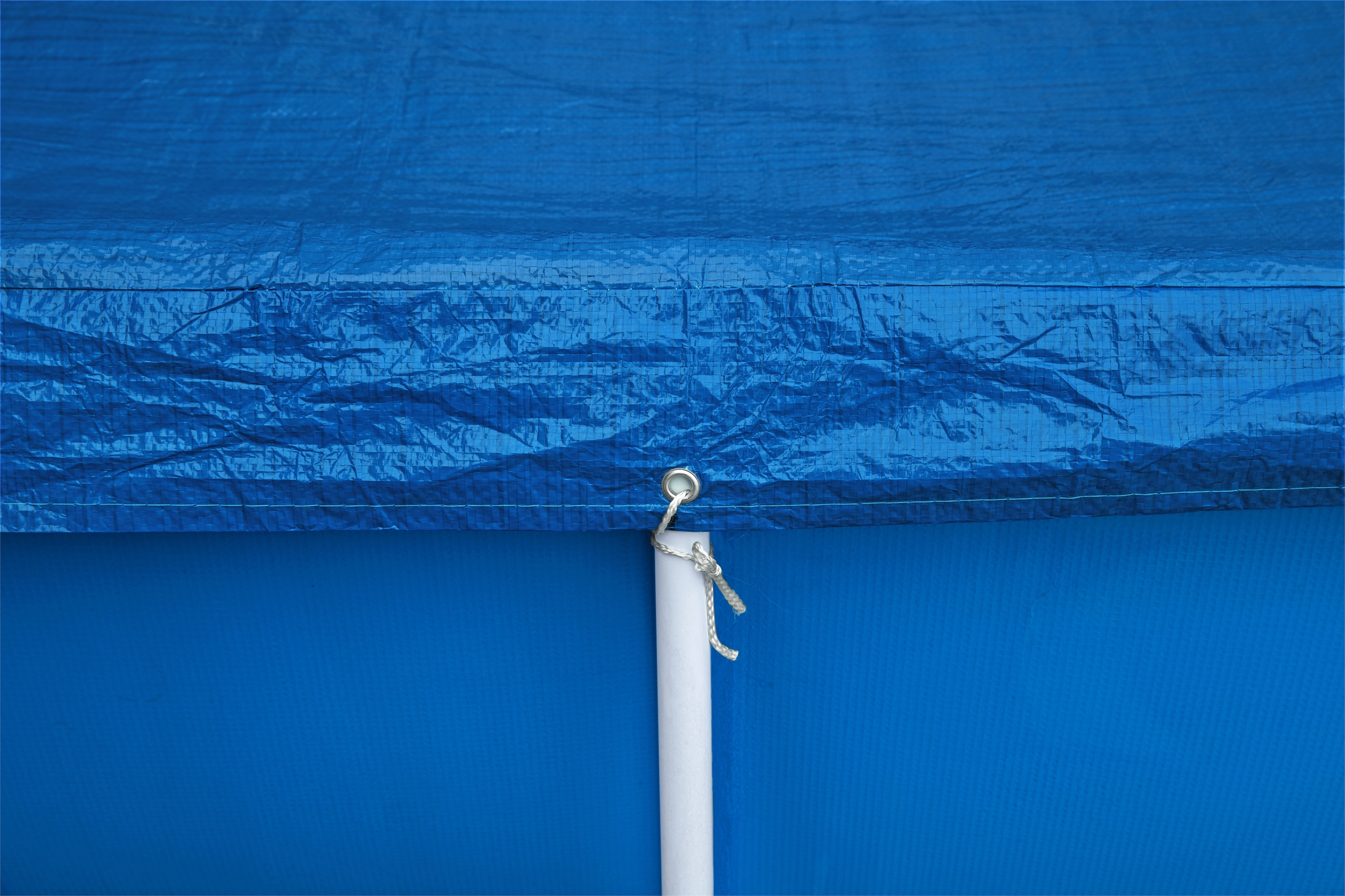 Blaue Plane mit weißer Stange und Öse. Die Plane ist zerknittert und hat einen blauen Hintergrund.